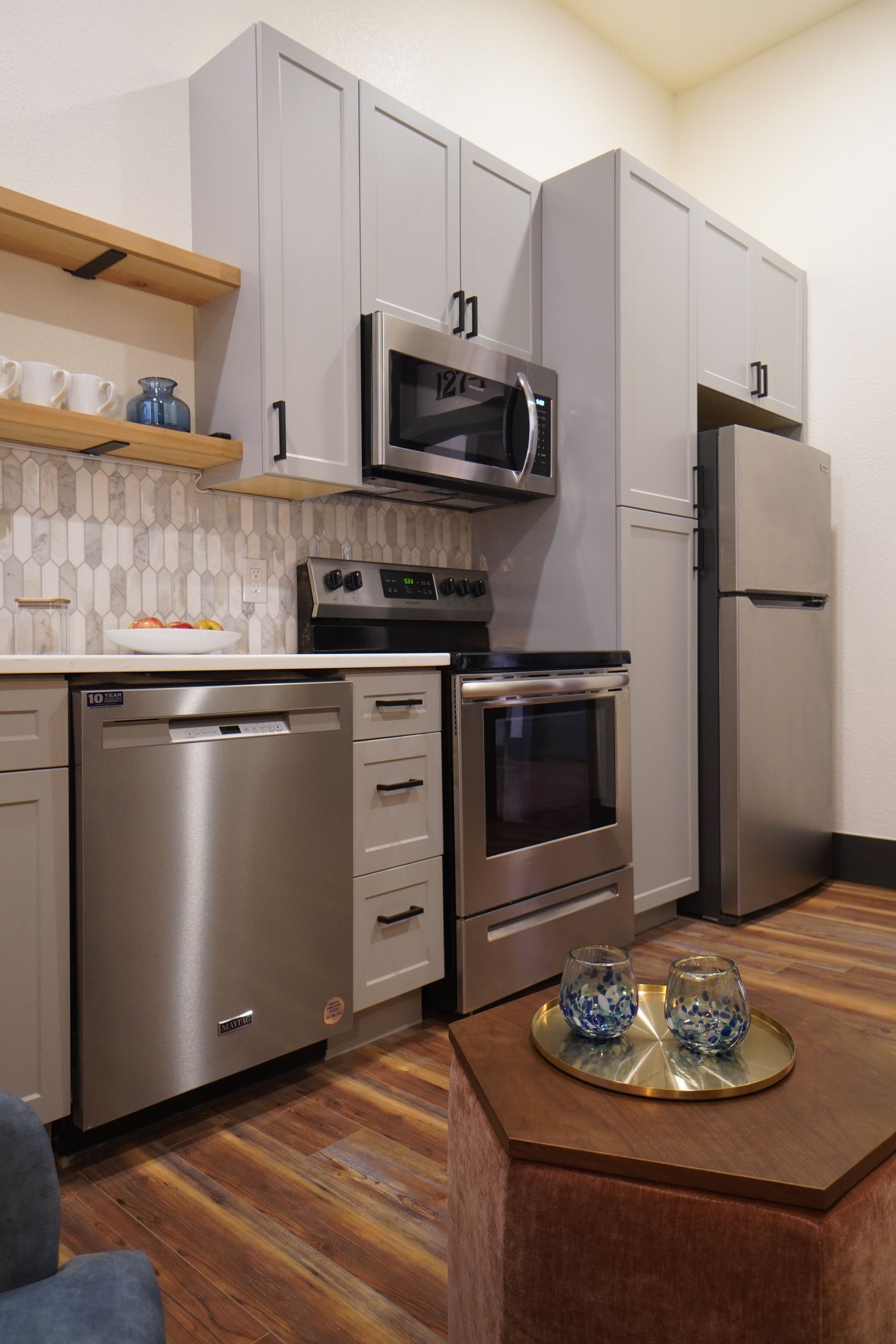 Modern kitchen with gray cabinets, stainless steel appliances, and wood floors.