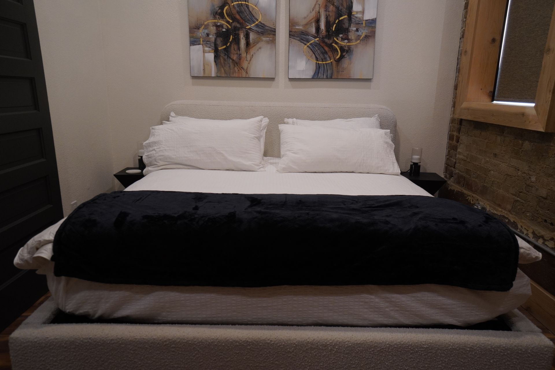 Bedroom with bed, white sheets, black blanket, two pillows, and artwork above.