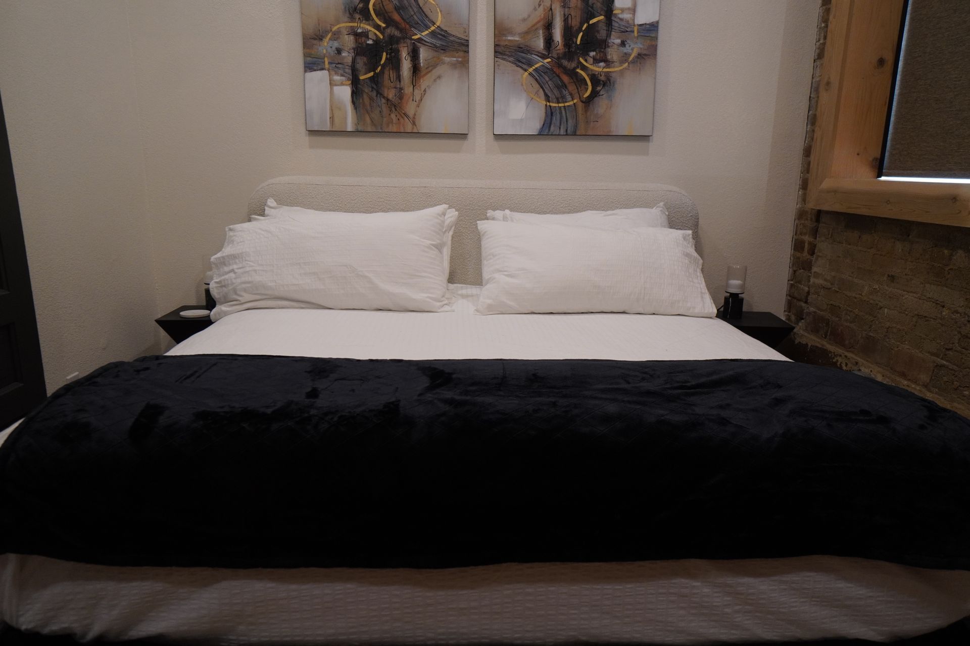 Bed with white linens, two pillows, and a dark blue blanket, with two abstract wall art pieces above.