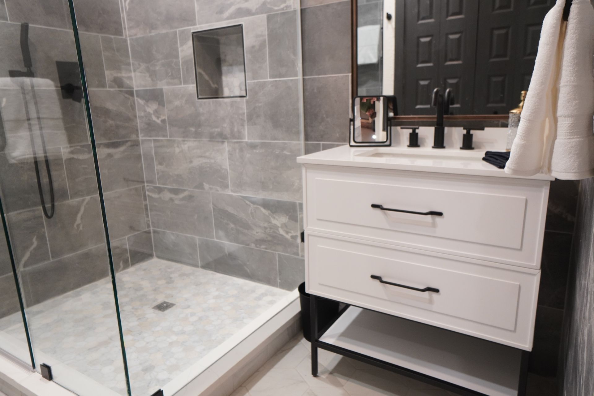 Modern bathroom with a white vanity, grey tile shower, and black fixtures.