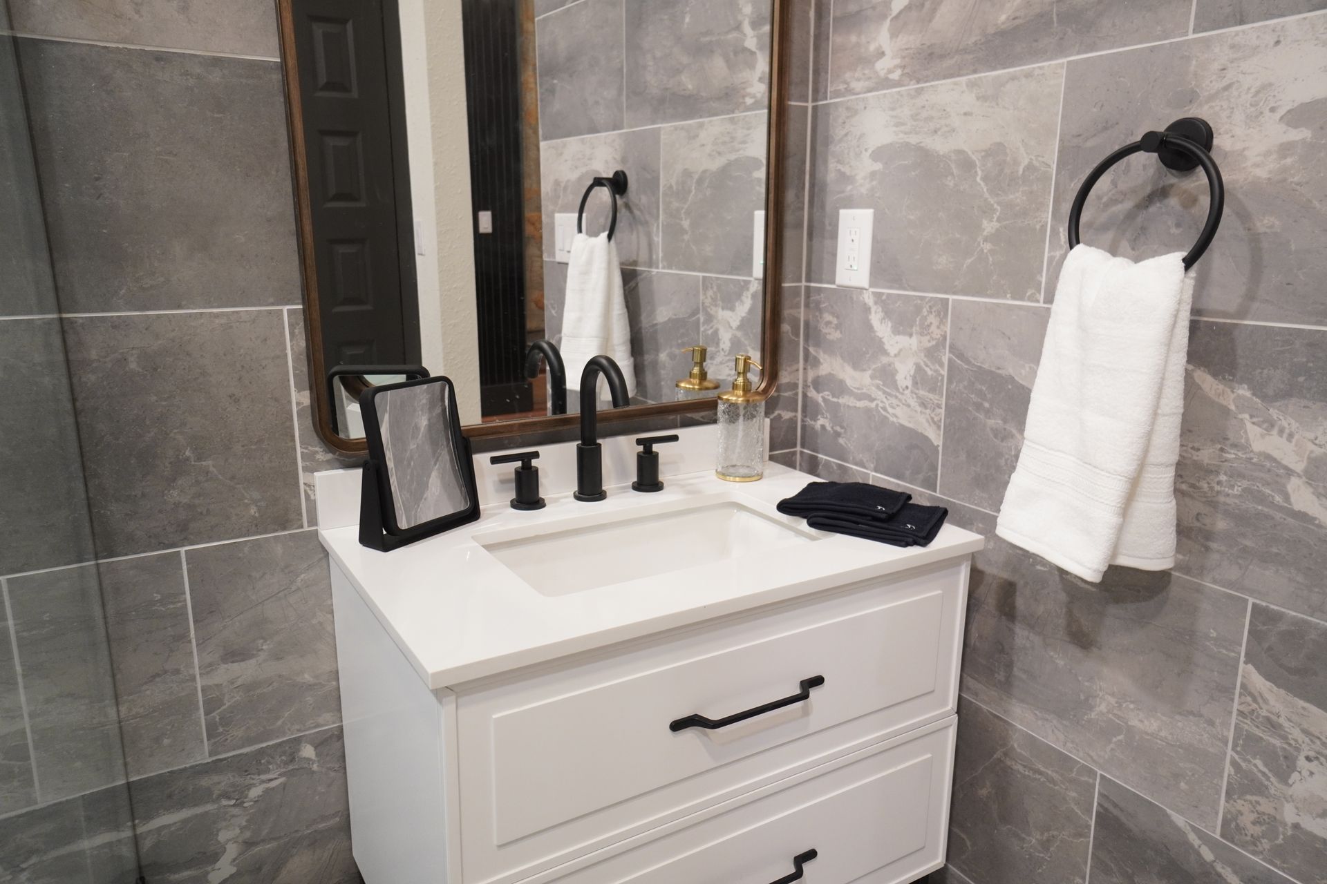 Bathroom vanity with white cabinet, black fixtures, and gray tile backdrop.