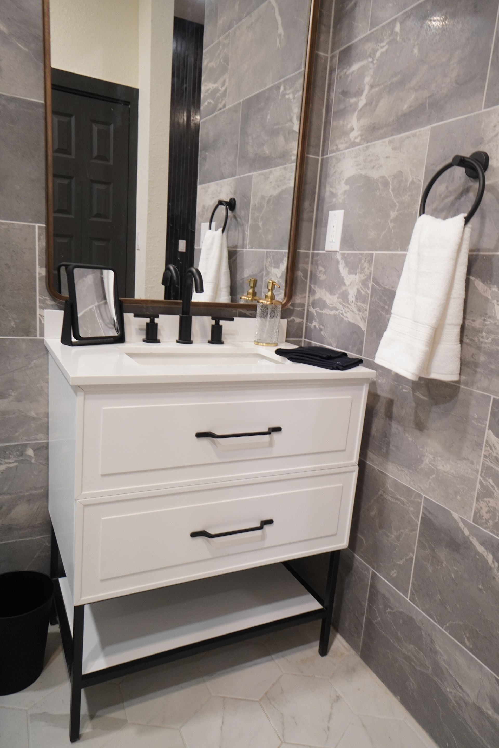 White bathroom vanity with black hardware against gray tiled wall; black accents.
