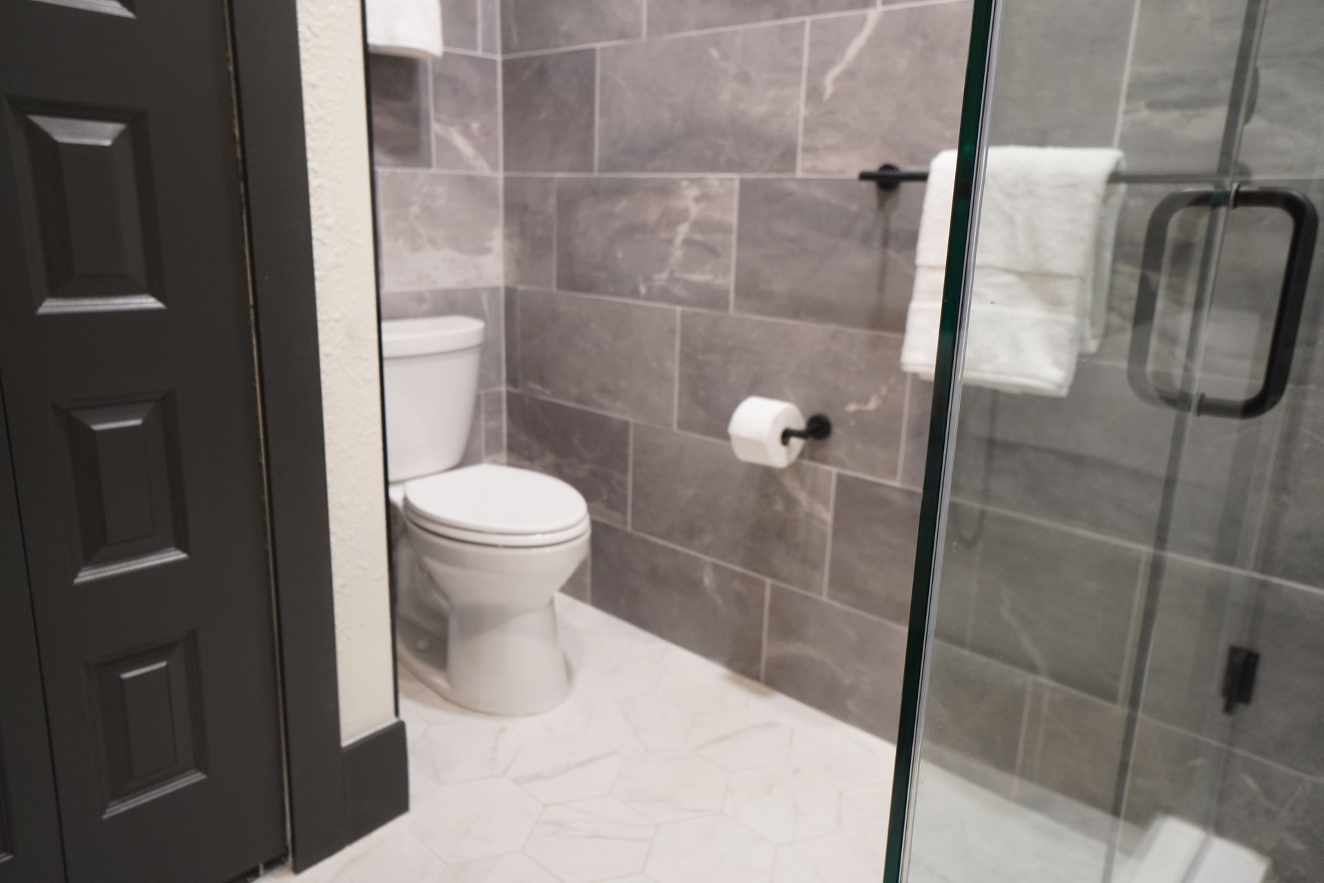 Bathroom with gray tiled walls, white toilet, and glass shower door.