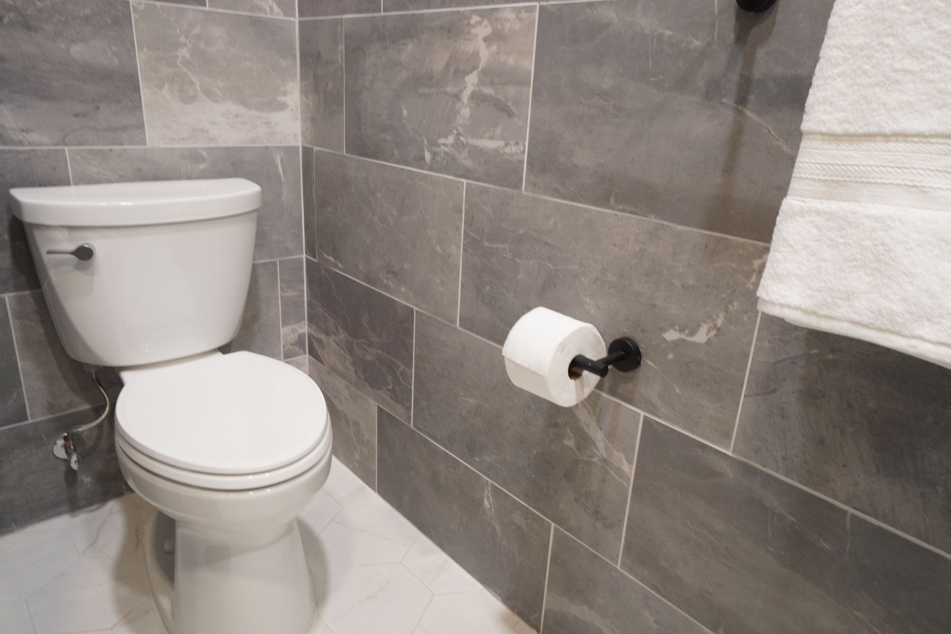 Bathroom with gray tiled walls, white toilet, and a roll of toilet paper.