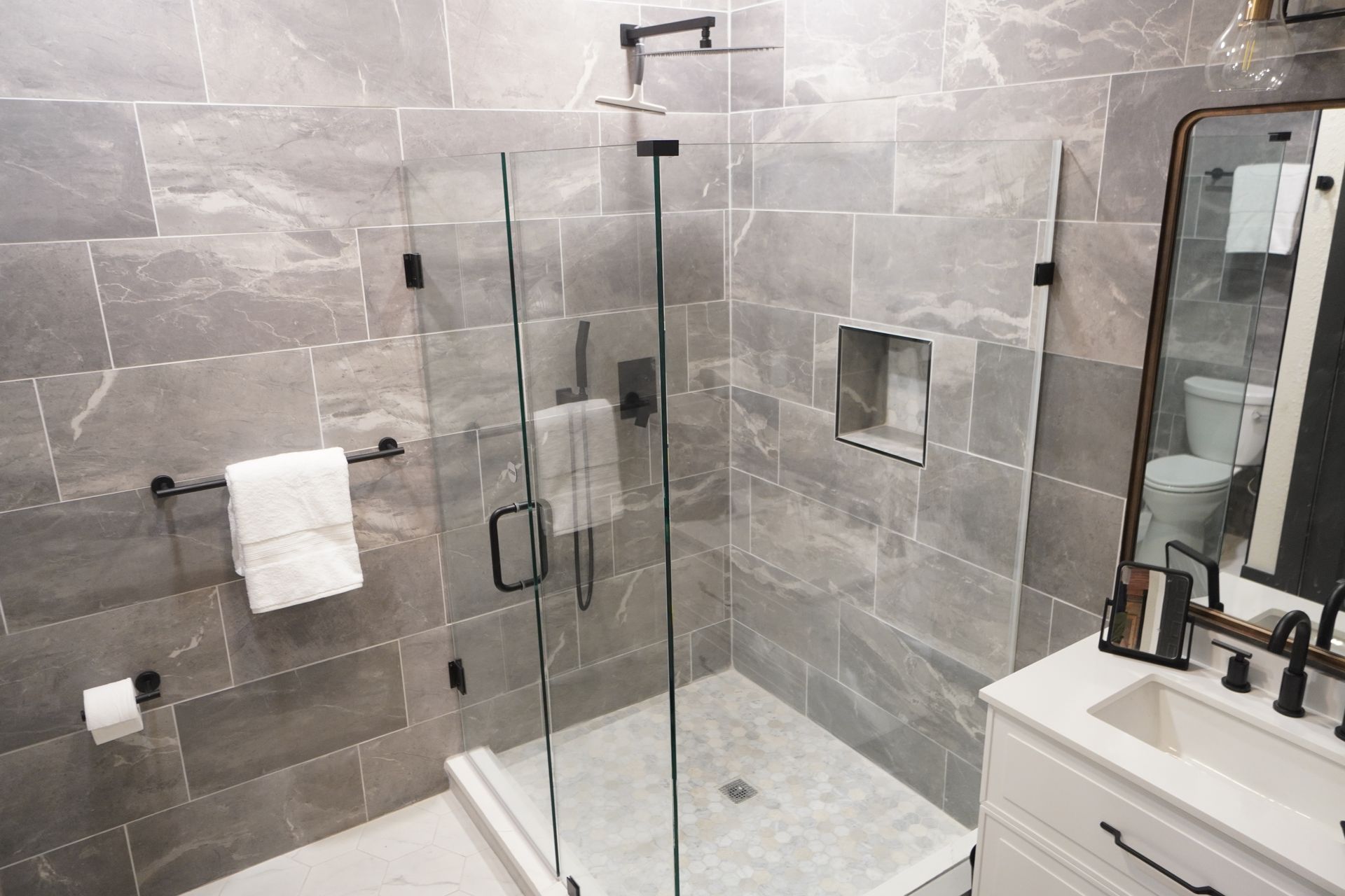 Modern bathroom with gray tile, glass shower, and white vanity.