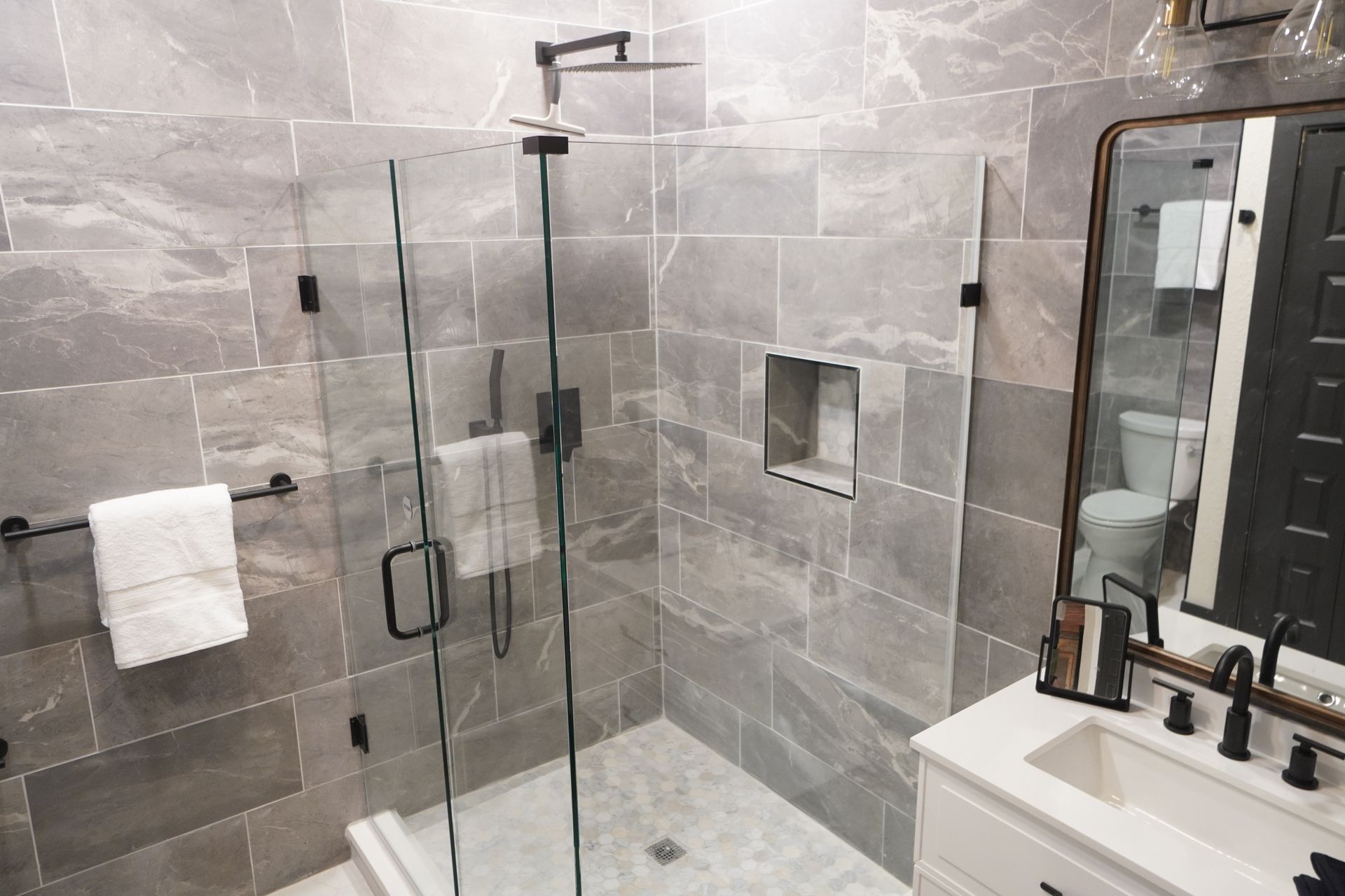 Modern bathroom with grey tile shower, glass doors, and black fixtures.