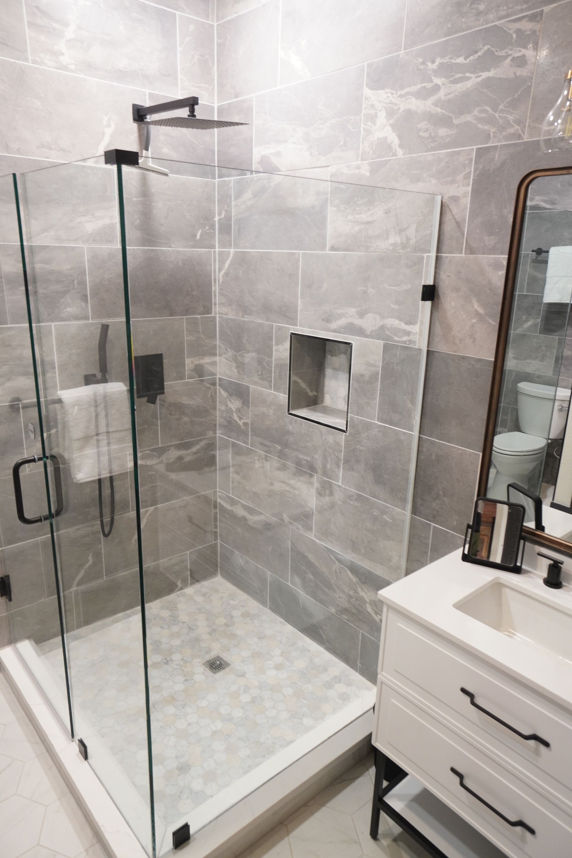 Modern bathroom with gray tile shower, glass door, and white vanity.