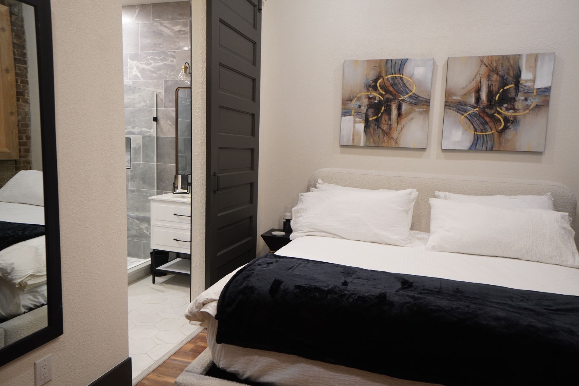 Bedroom with open black door revealing a bathroom. Bed has white bedding and a black throw.