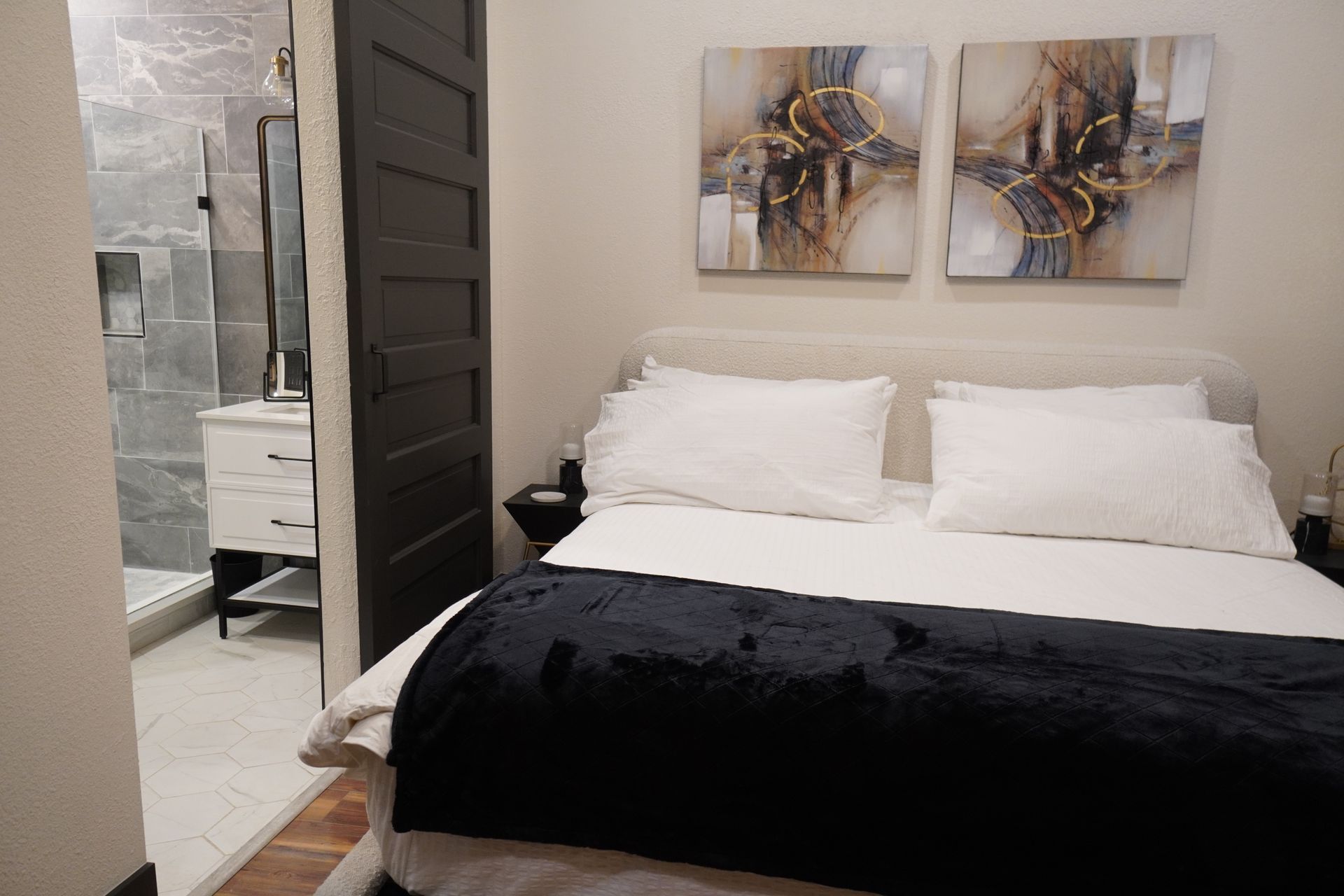 Bedroom with bed, art, and bathroom partially visible. Dark door and navy blanket.