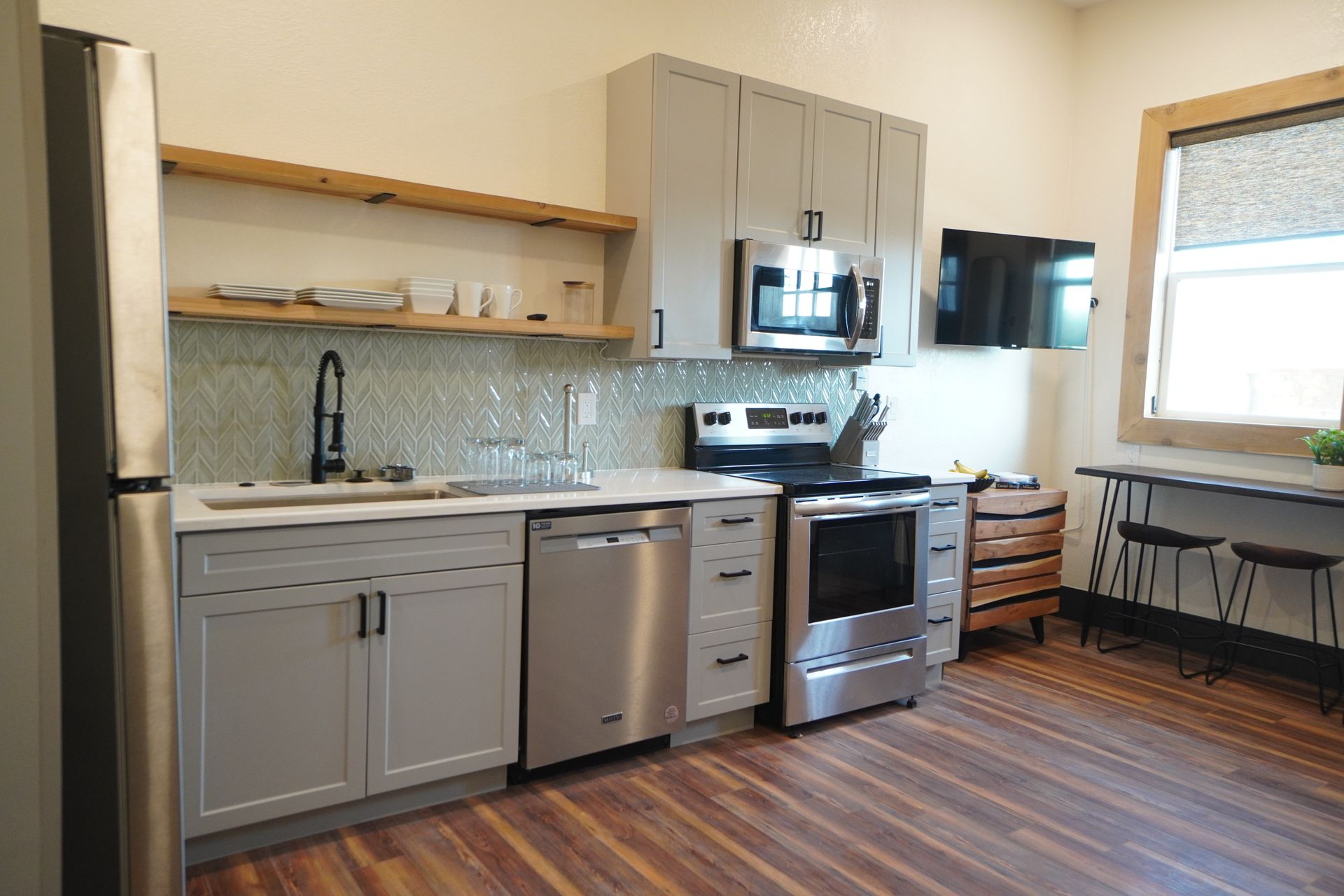Modern kitchen with gray cabinets, stainless steel appliances, and wood floors.