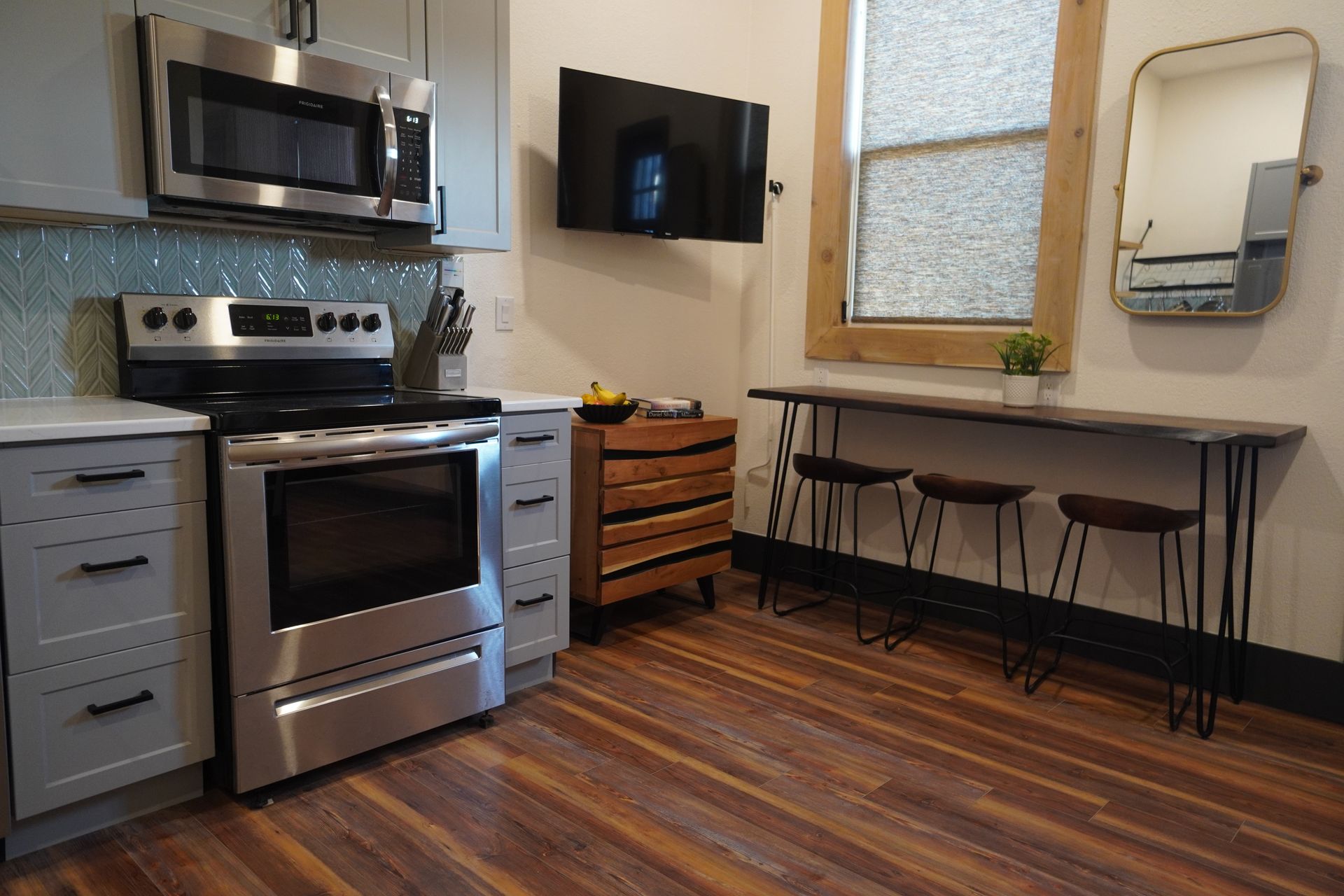 A small kitchen with stainless steel appliances, grey cabinets, and a wooden bar table with stools.