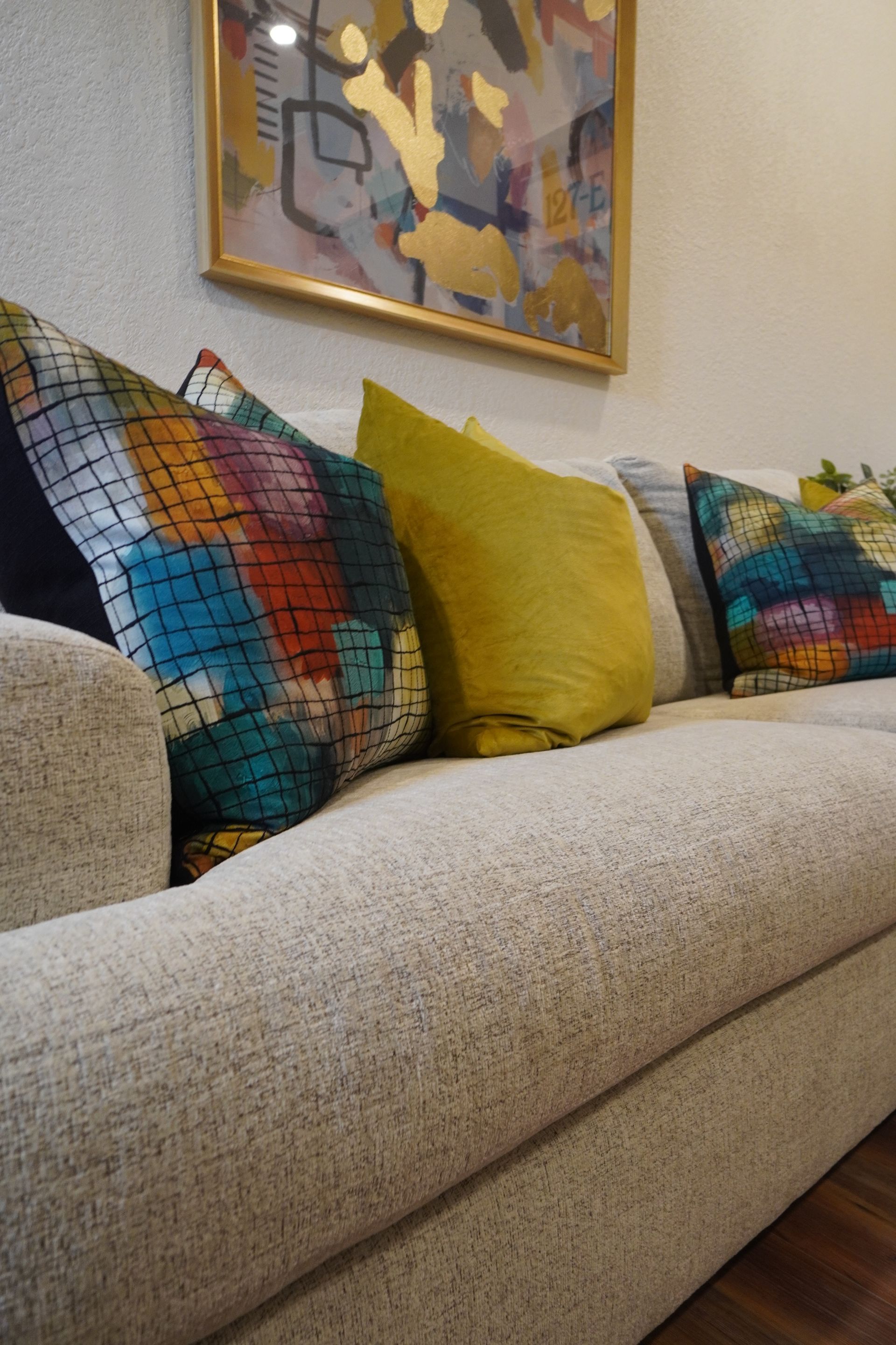 Beige sofa with colorful pillows beneath a gold-framed abstract painting.