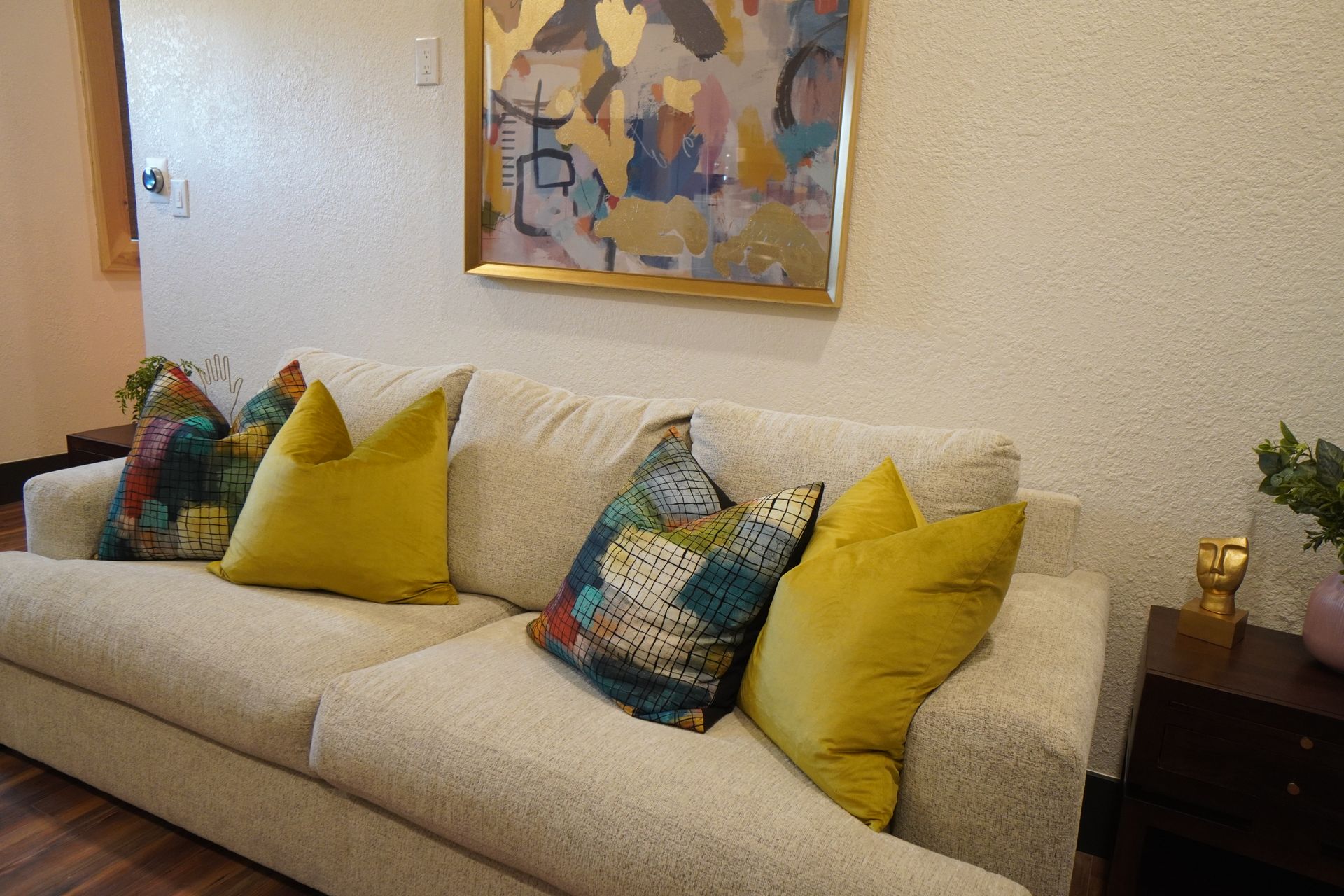 Beige couch with yellow and patterned pillows, artwork hanging above.