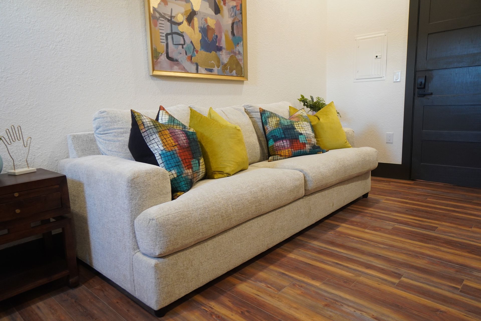 Beige couch with colorful throw pillows in a room with hardwood floors and a painting.