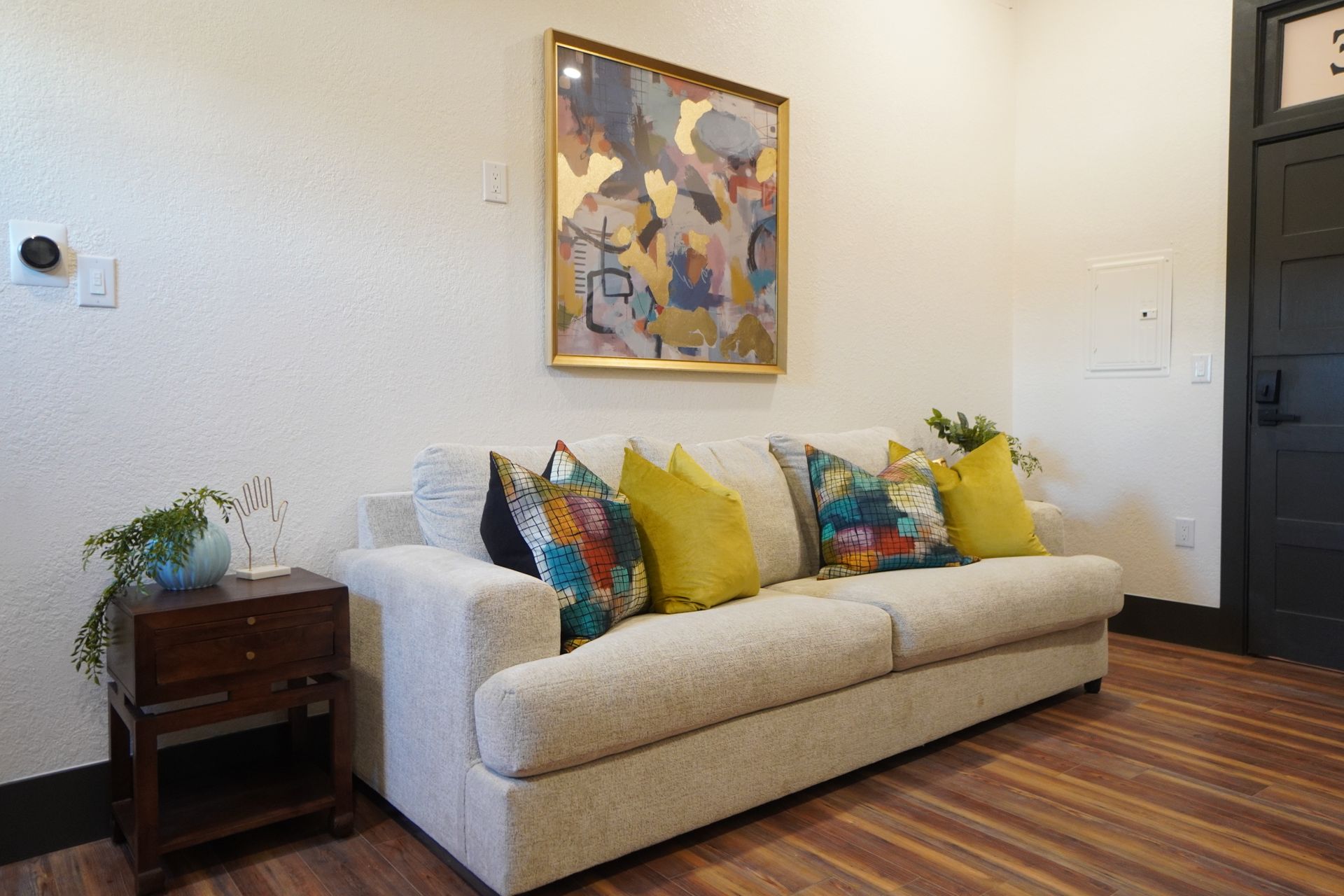 Cream sofa with colorful pillows and art hanging in a room with a wood floor.