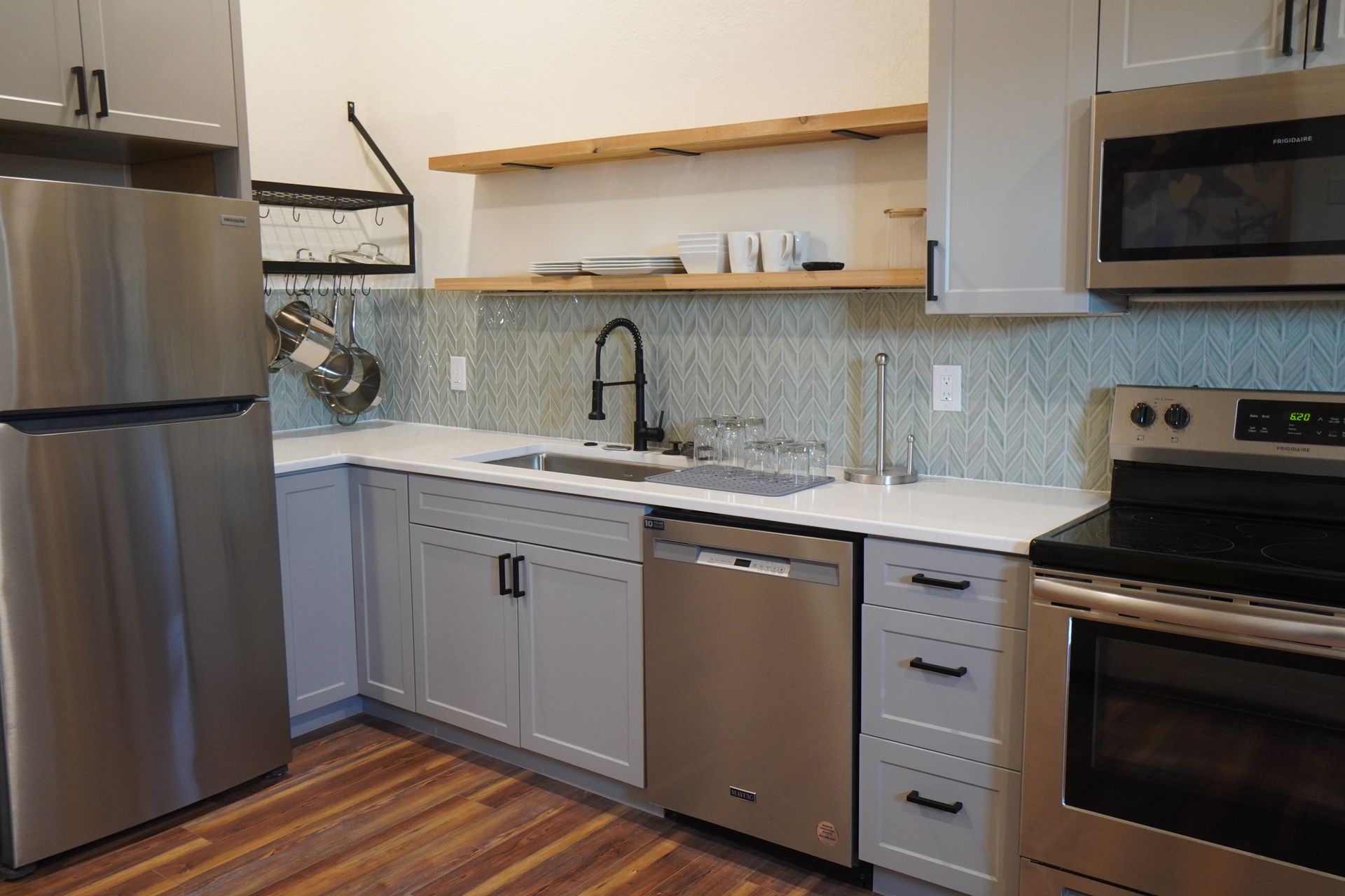 Modern kitchen with gray cabinets, stainless steel appliances, and wood shelves.