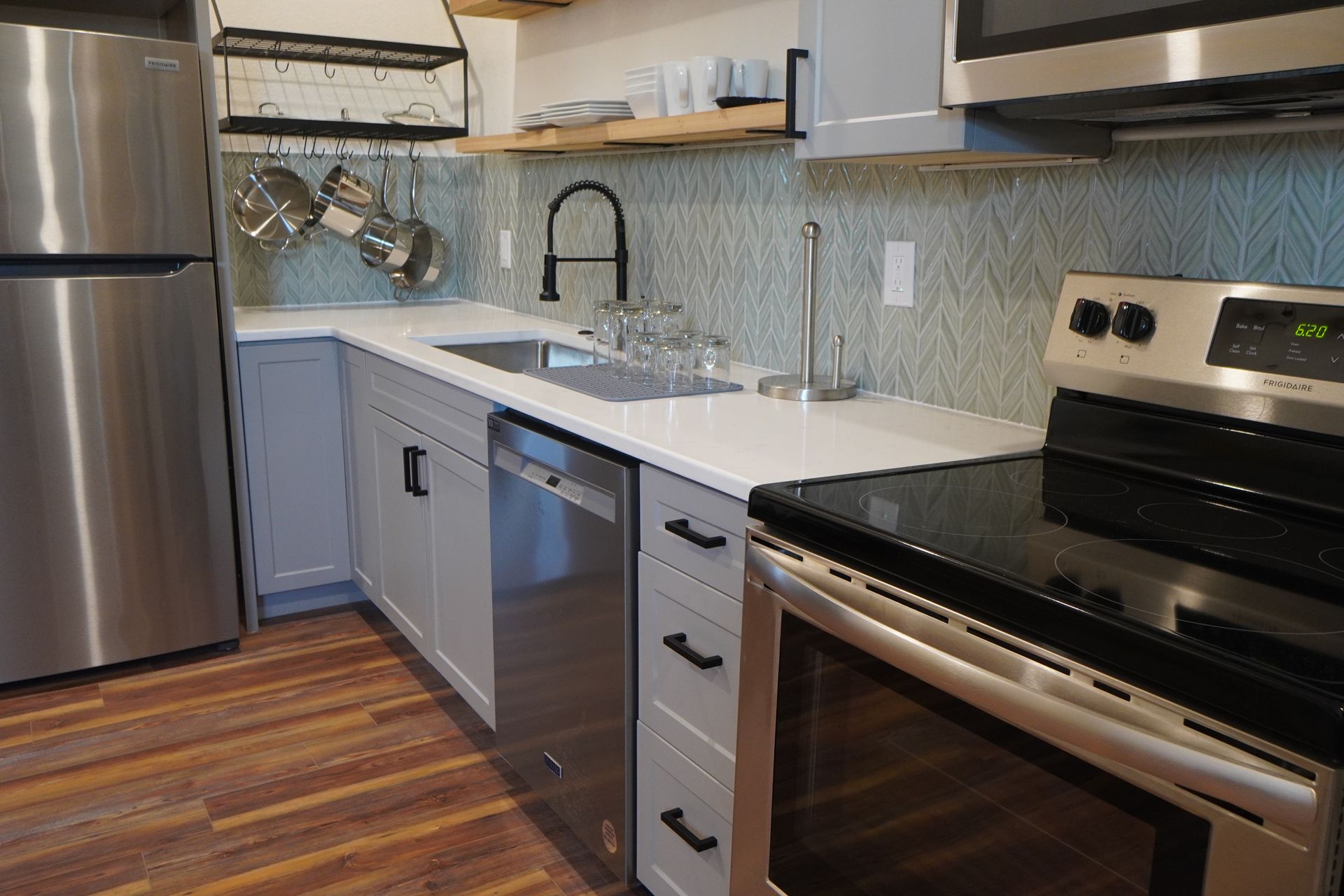 Kitchen with stainless steel appliances, light blue cabinets, white countertop, and wooden floor.