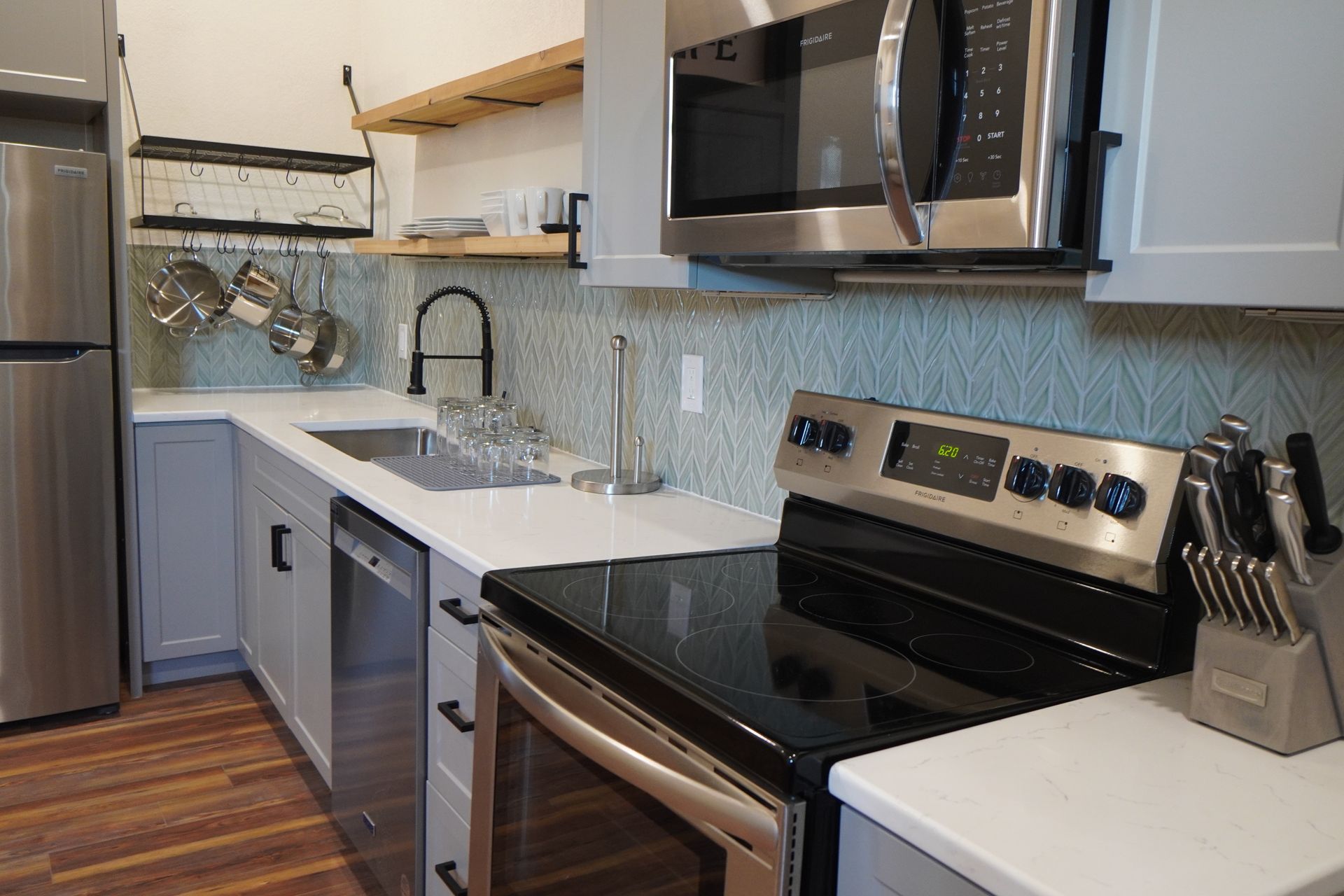 Modern kitchen with stainless steel appliances, gray cabinets, and light blue backsplash.