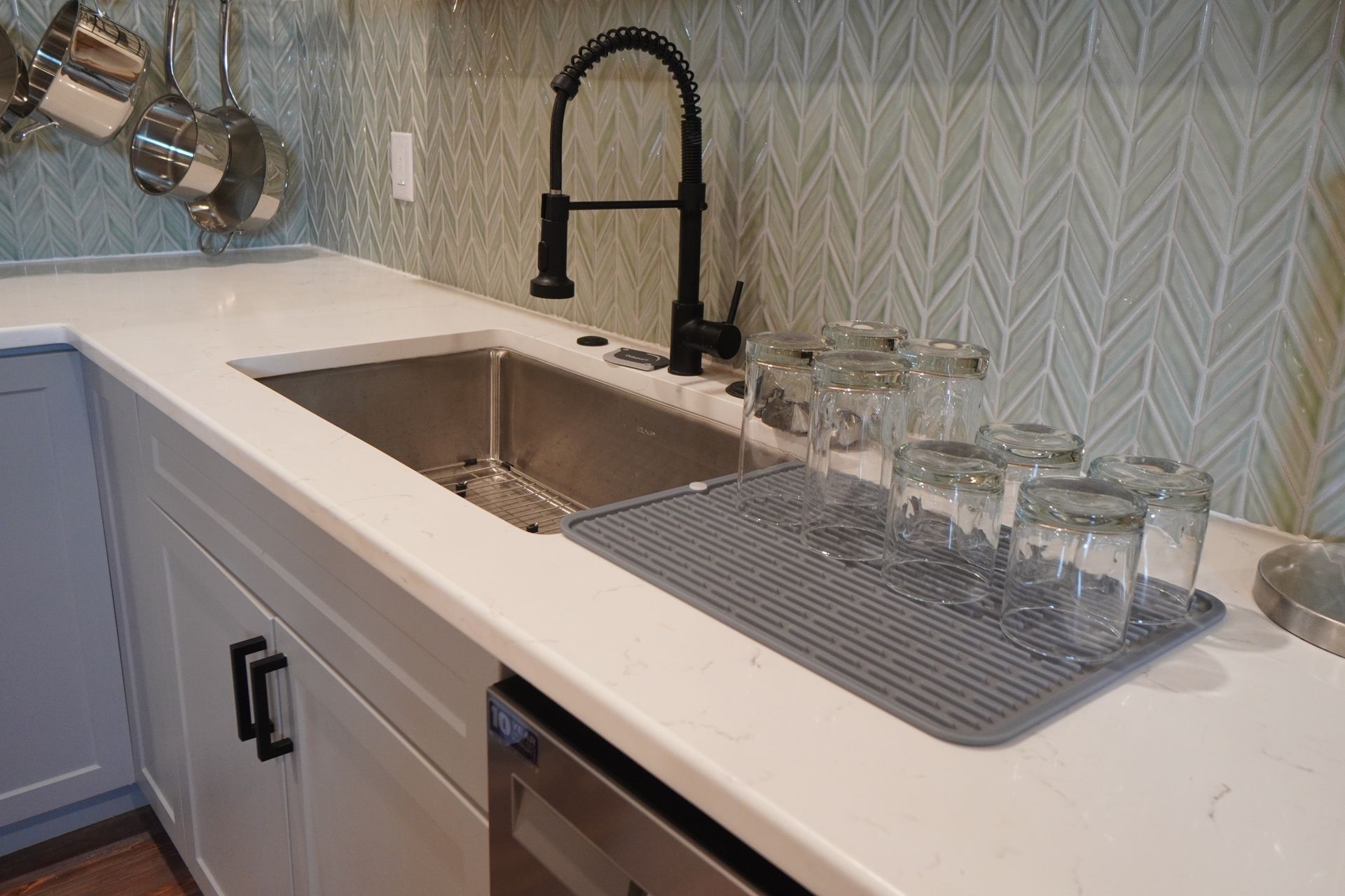 Kitchen sink with white countertop, black faucet, and glasses drying on a gray mat.