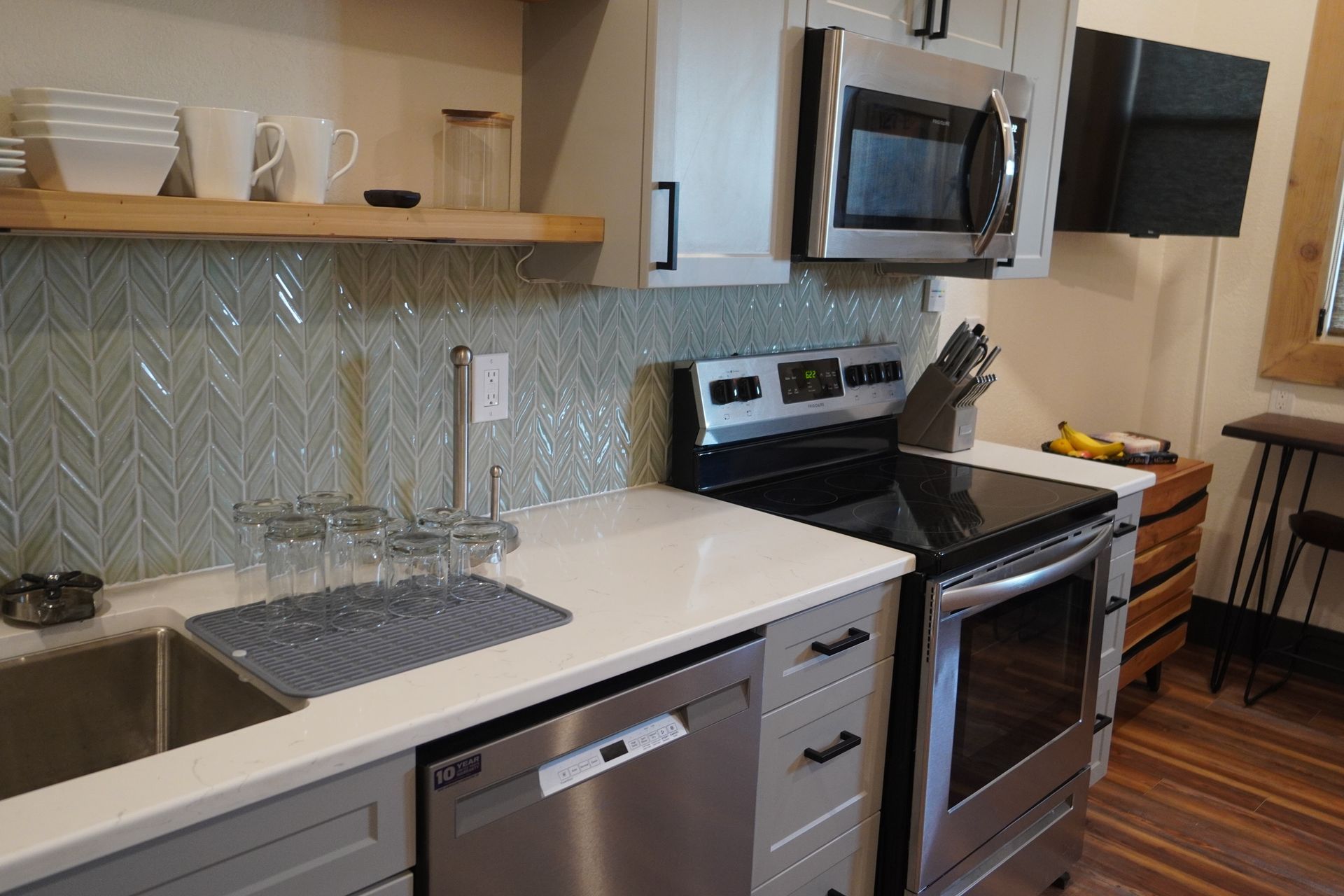 Modern kitchen with light gray cabinets, stainless steel appliances, and a tiled backsplash.