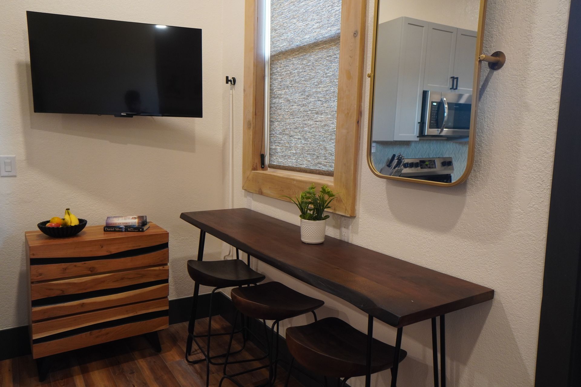 Room with TV, counter, stools, and mirror reflecting a kitchen area. Wooden details and neutral walls.