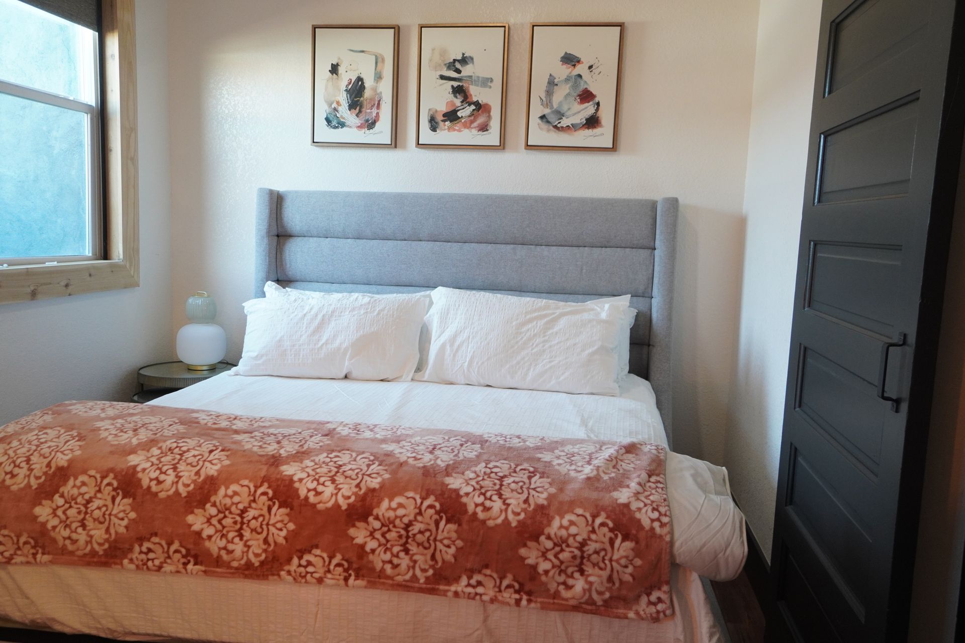 Bedroom with bed, headboard, art, and a dark door. Orange and white bedding. Light blue headboard.