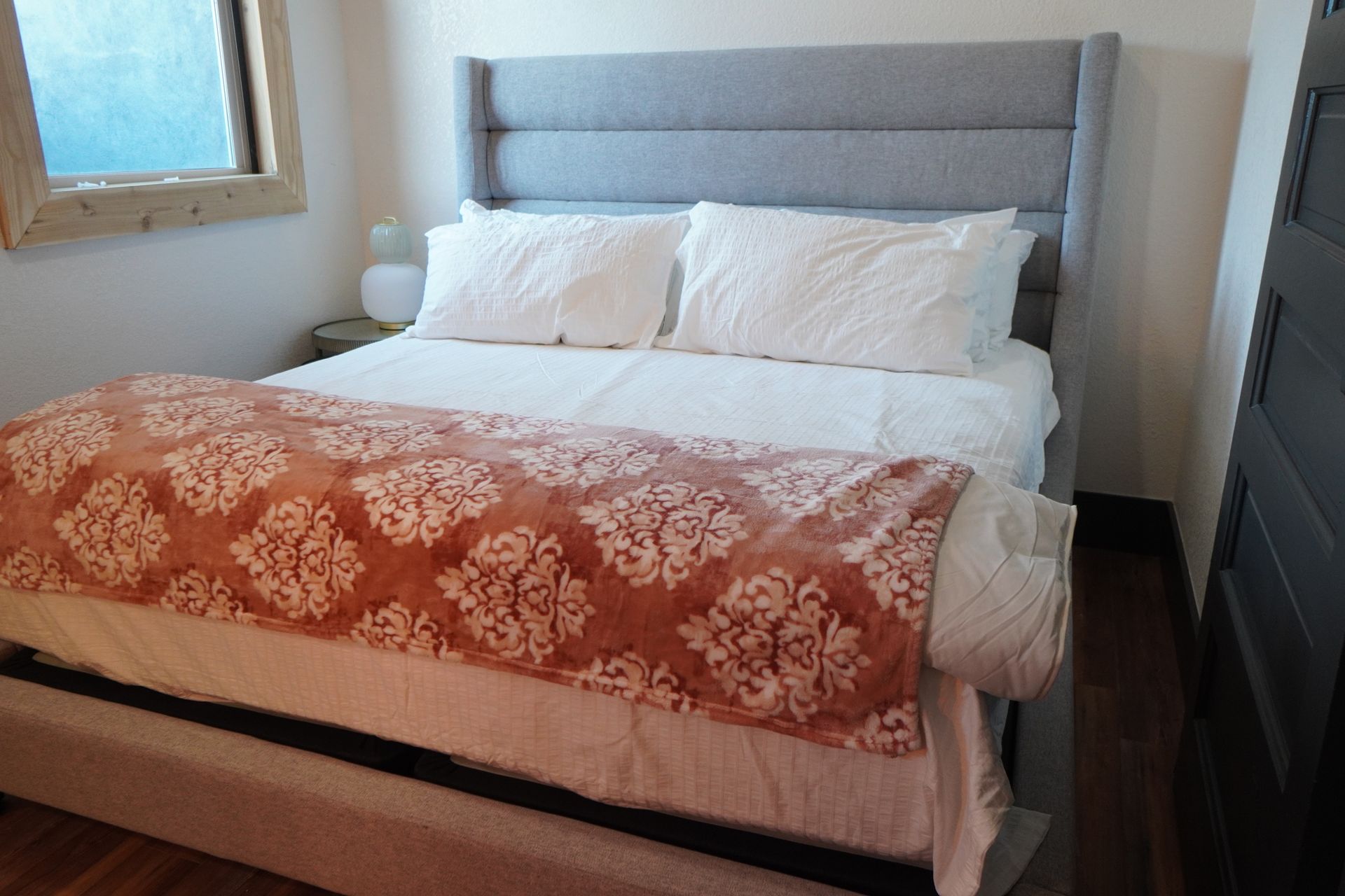 Bedroom with a gray upholstered headboard, white bedding, and a patterned orange and white blanket.