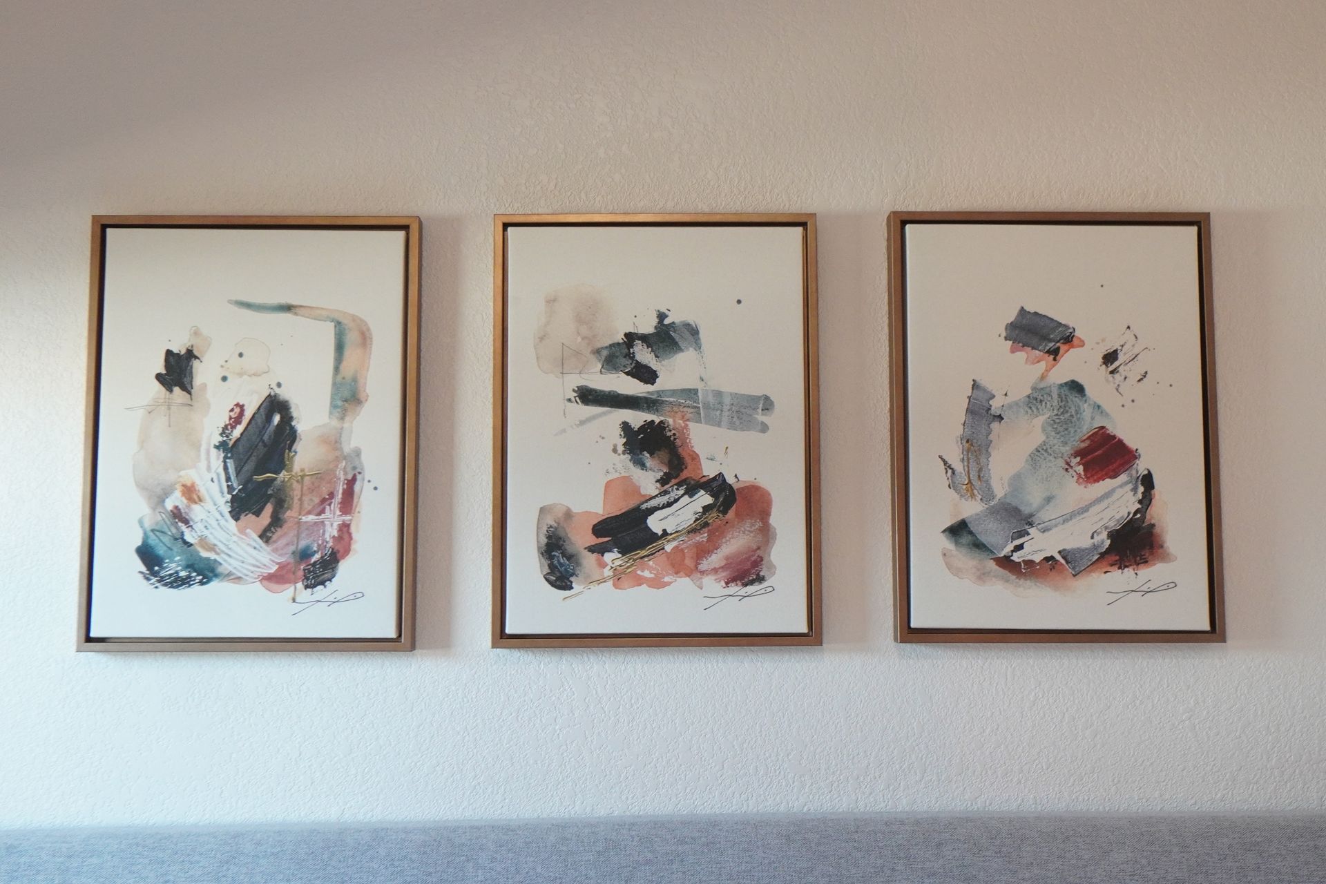 Three abstract watercolor paintings in wooden frames, displayed on a white wall.
