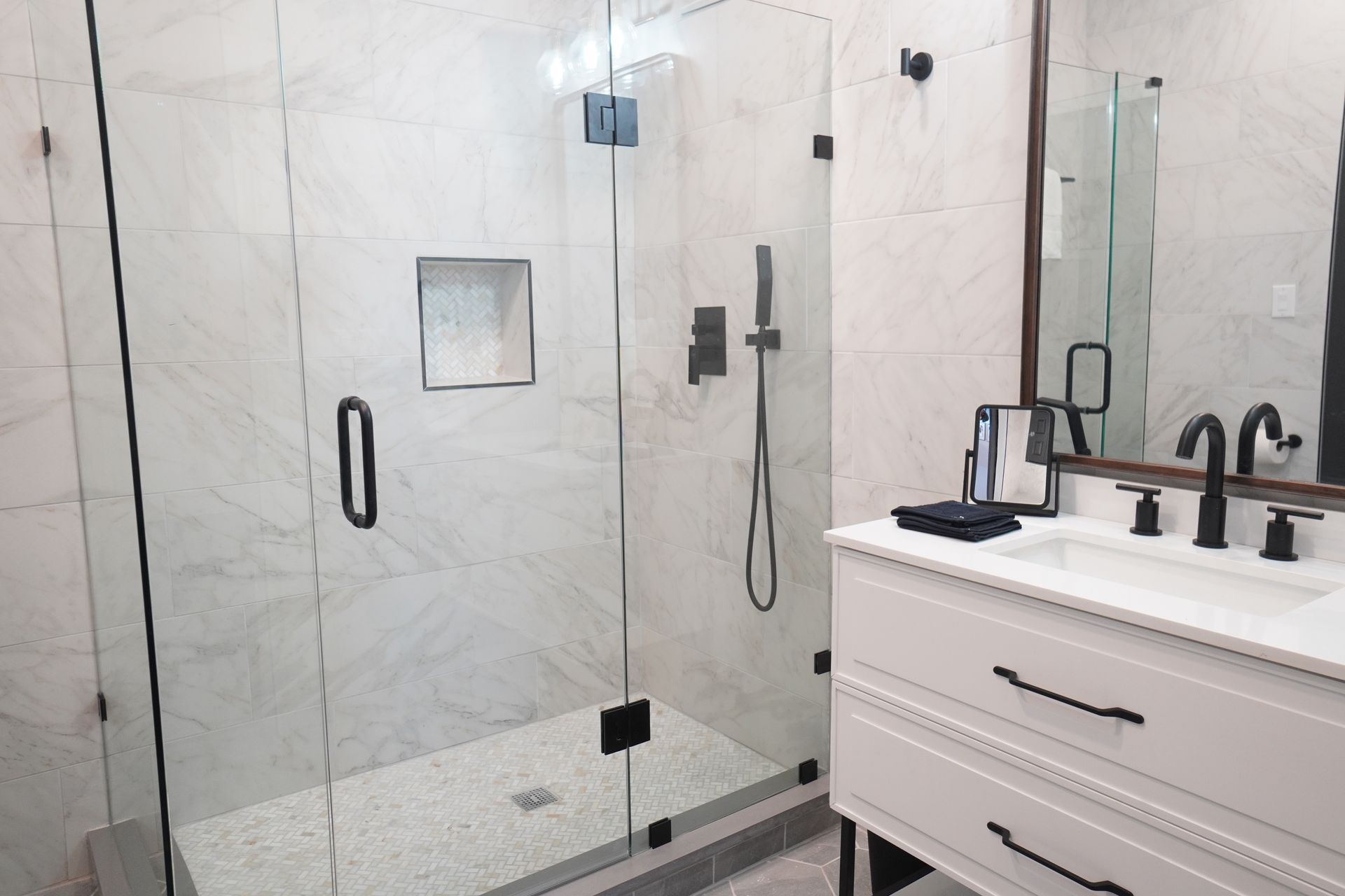 Modern bathroom with glass shower, white vanity, and black fixtures.