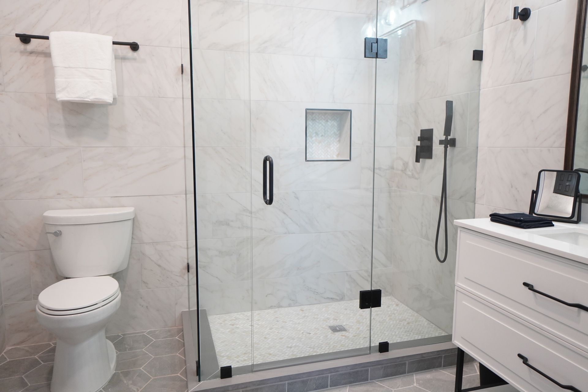 Bathroom with white marble tile, glass shower, toilet, and vanity.