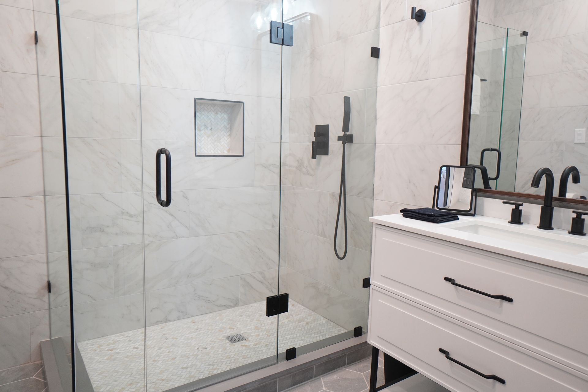 Bathroom with a glass shower enclosure, white marble tile, and black fixtures.