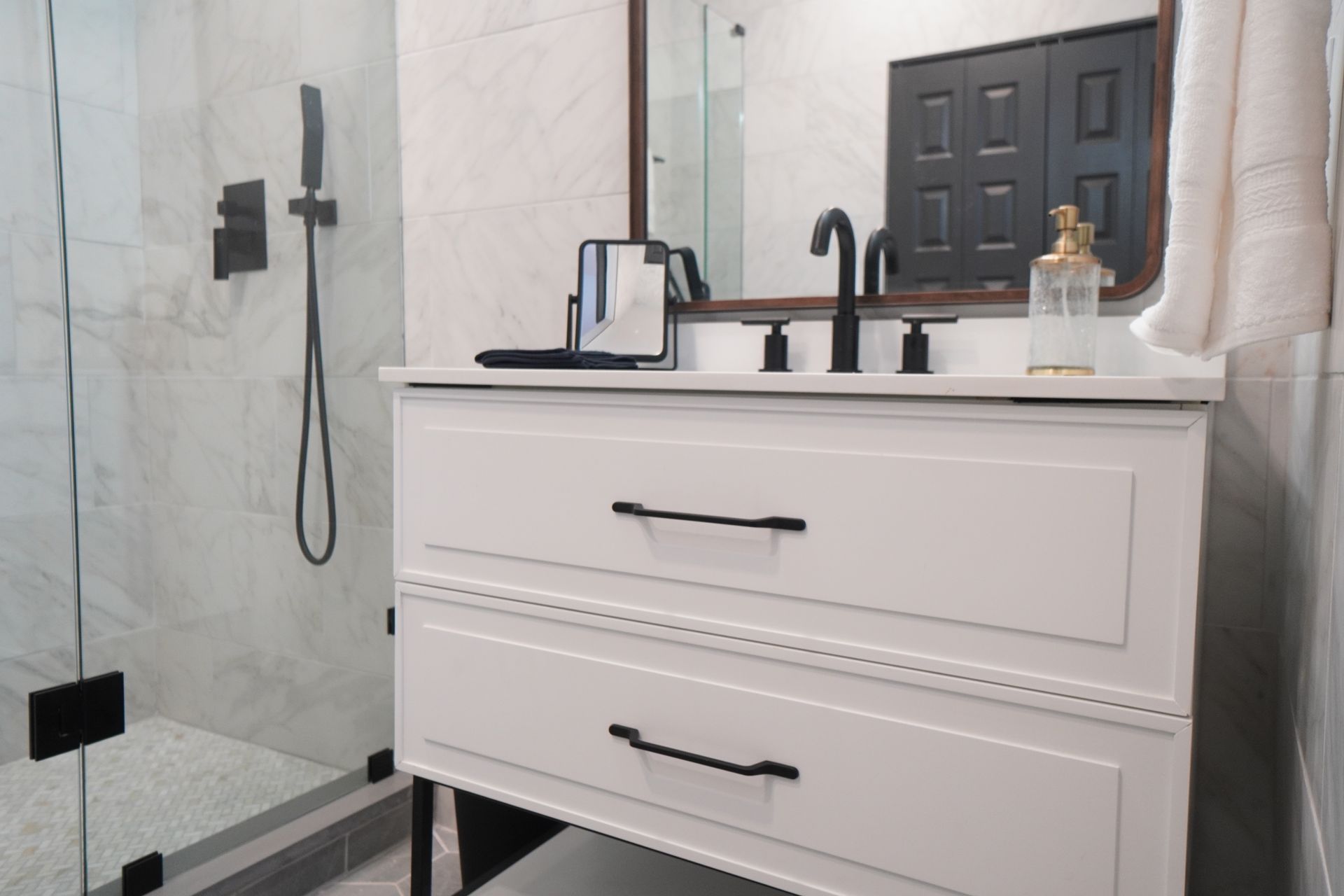 White bathroom vanity with black hardware, a shower, and a mirror.