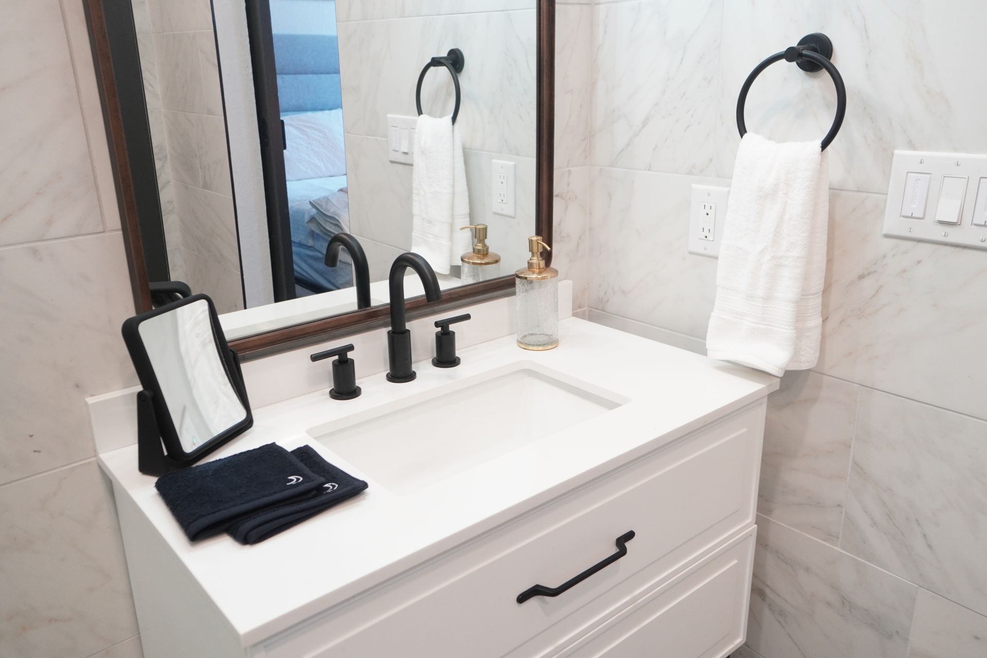 White bathroom vanity with black fixtures, mirror, and accessories. A white hand towel hangs on a black ring.