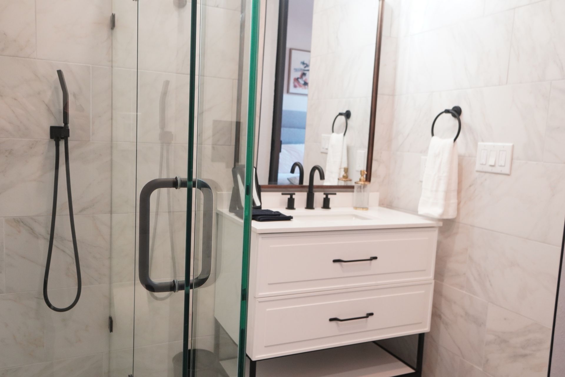 Modern bathroom with white vanity, black fixtures, glass shower, and marble tile walls.