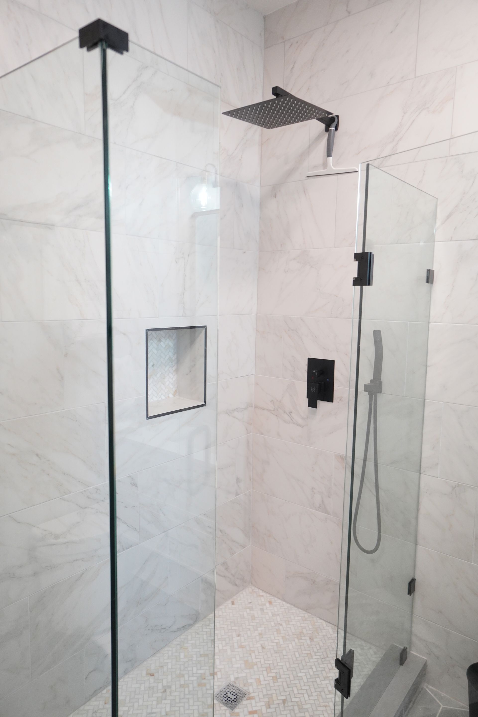 Modern shower with glass doors, black fixtures, and white marble-look tiles.