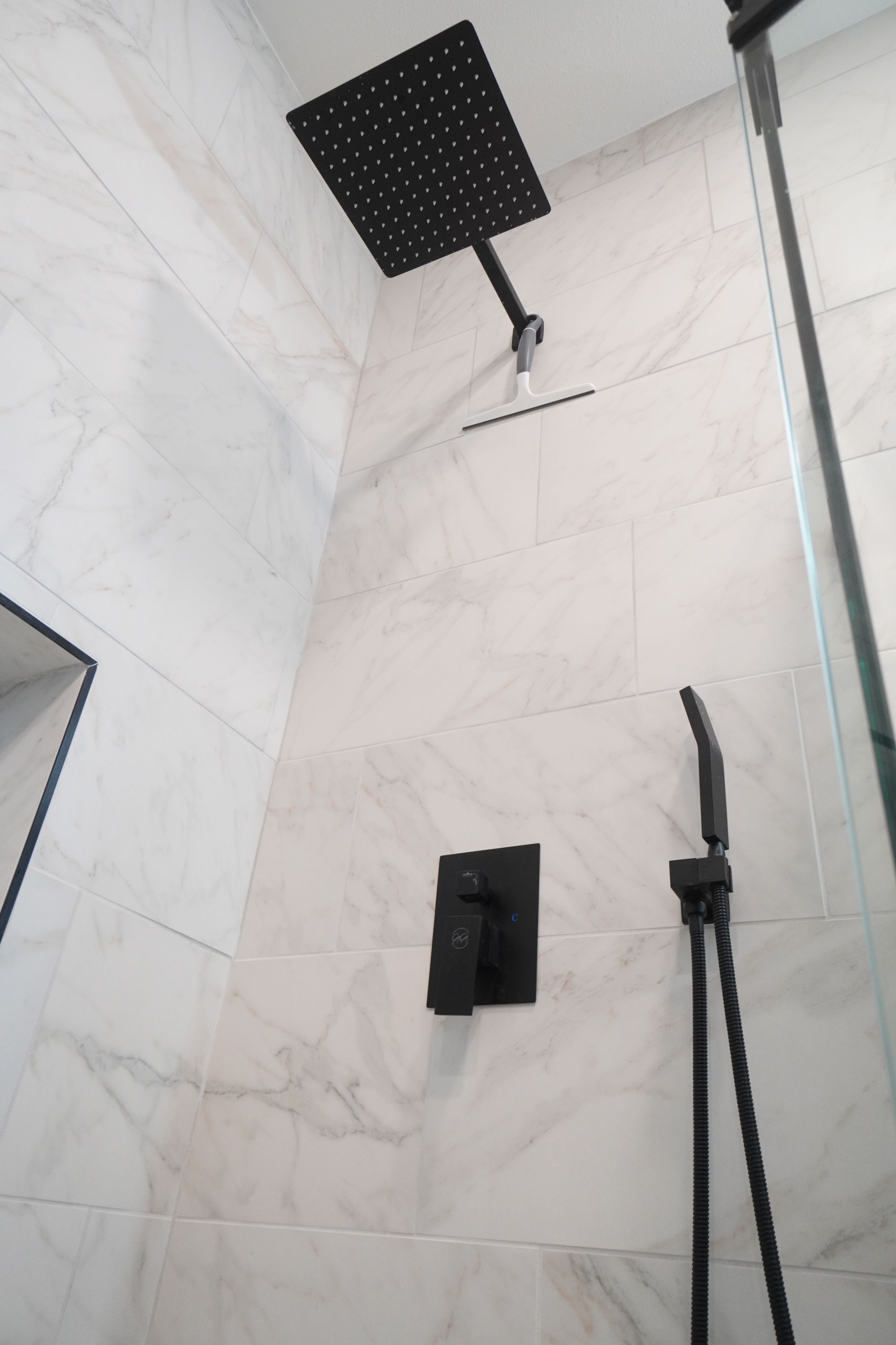 Black shower fixtures against marble tile in a bathroom.