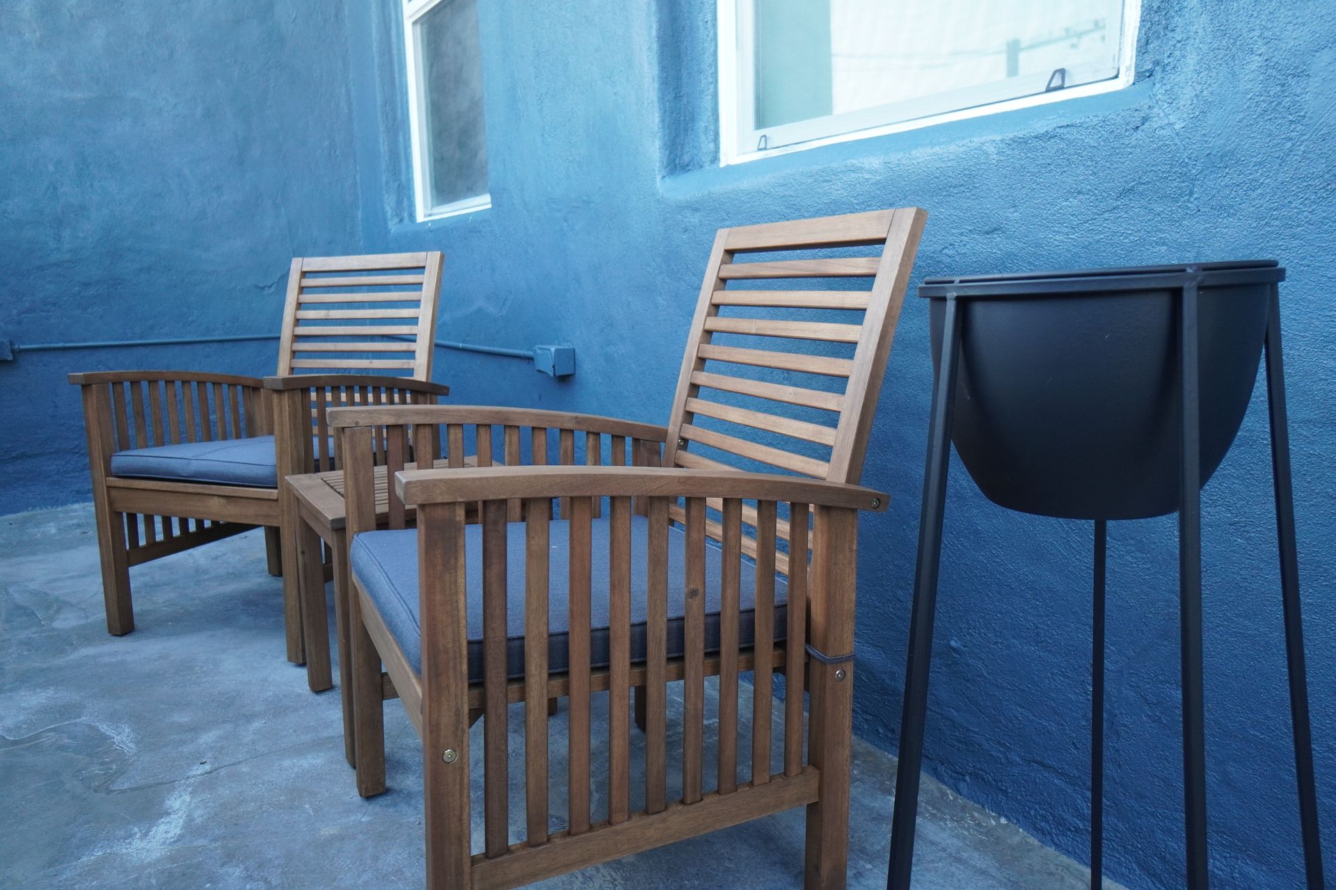 Two wooden chairs with blue cushions on a blue patio, black planter.