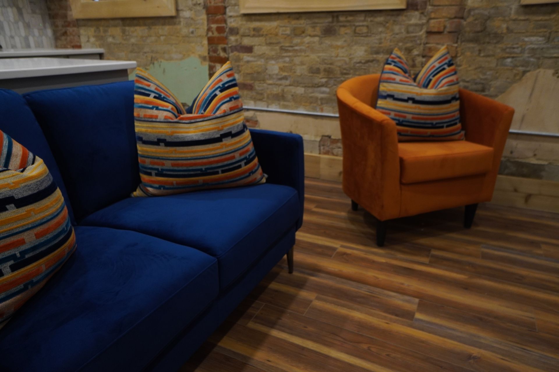 Blue sofa and orange armchair with striped pillows in a room with a brick wall and wooden floor.