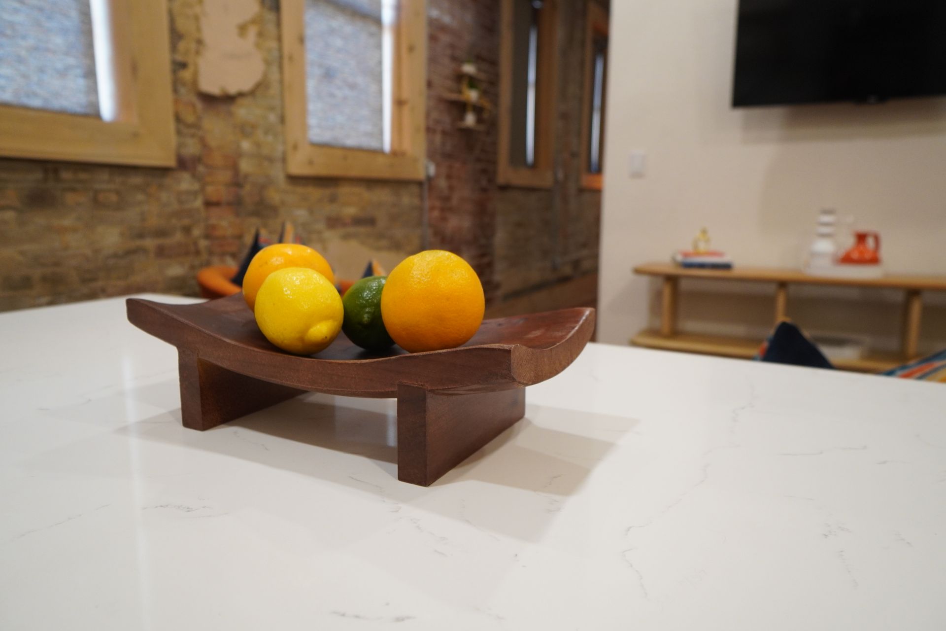 Fruit arrangement on a wooden tray atop a white countertop with brick wall backdrop.