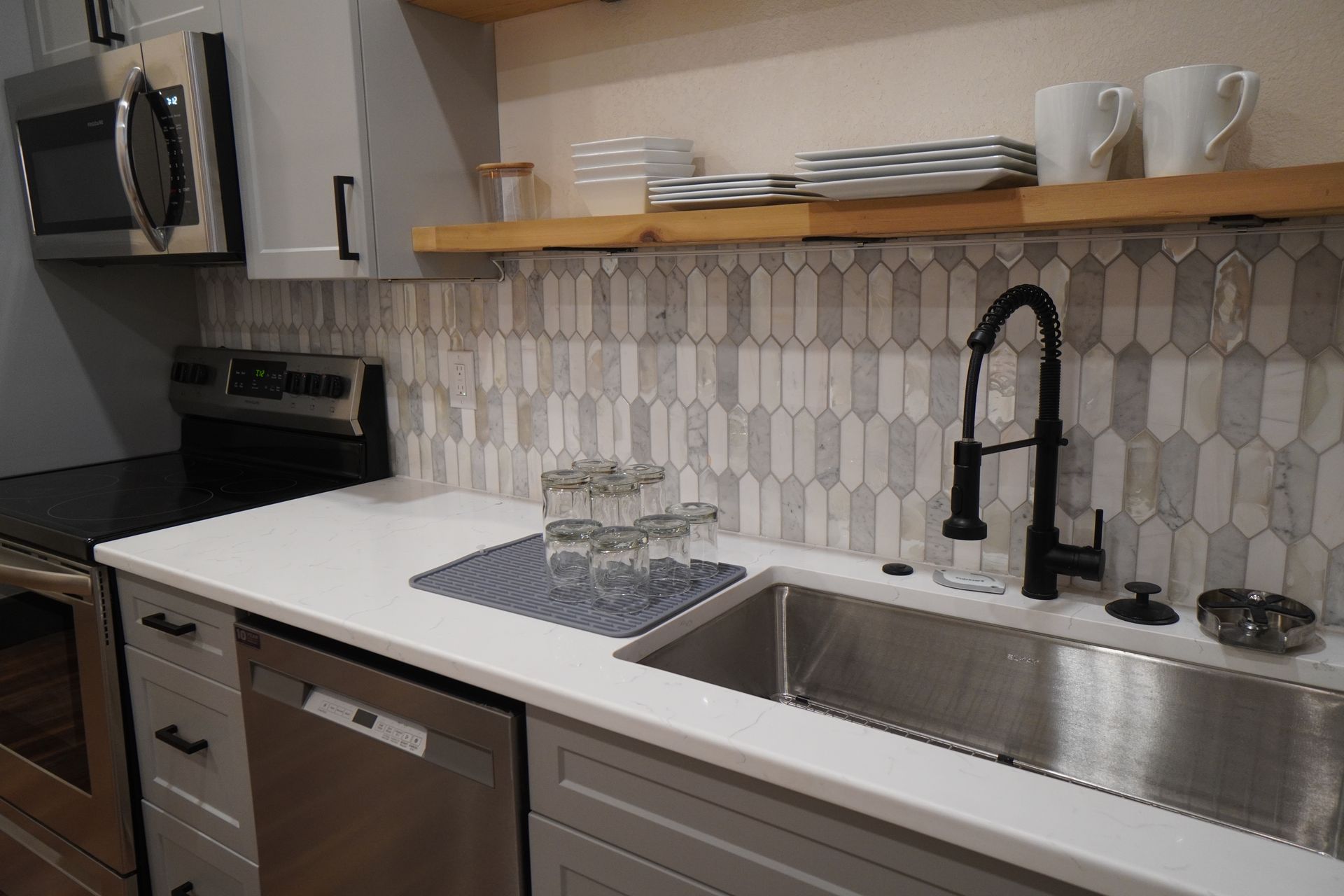 Kitchen with gray cabinets, stainless steel appliances, white countertop, and patterned backsplash.
