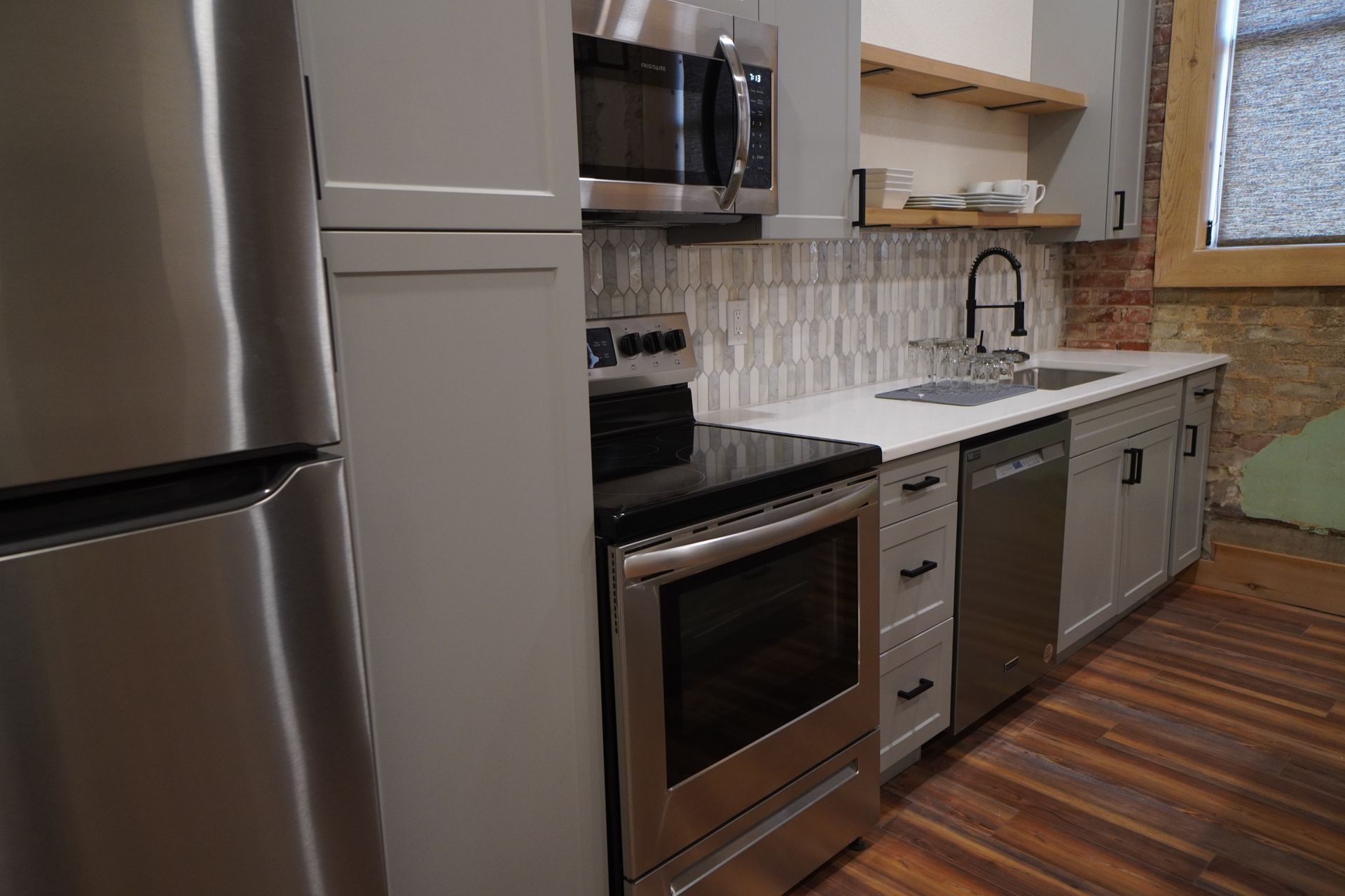 Modern kitchen with stainless steel appliances, gray cabinets, and wooden floors.