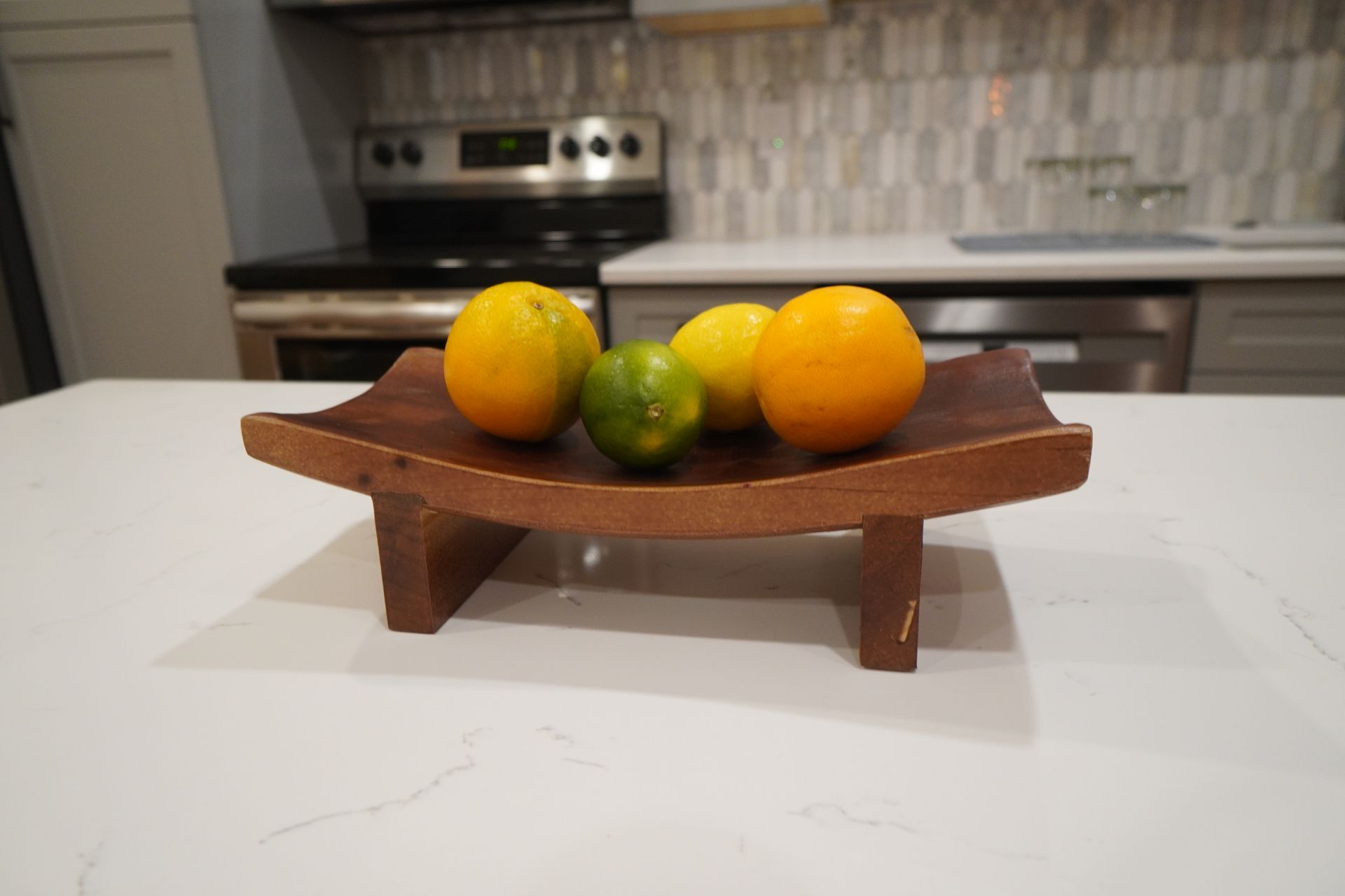Oranges and lime on a wooden tray in a kitchen.