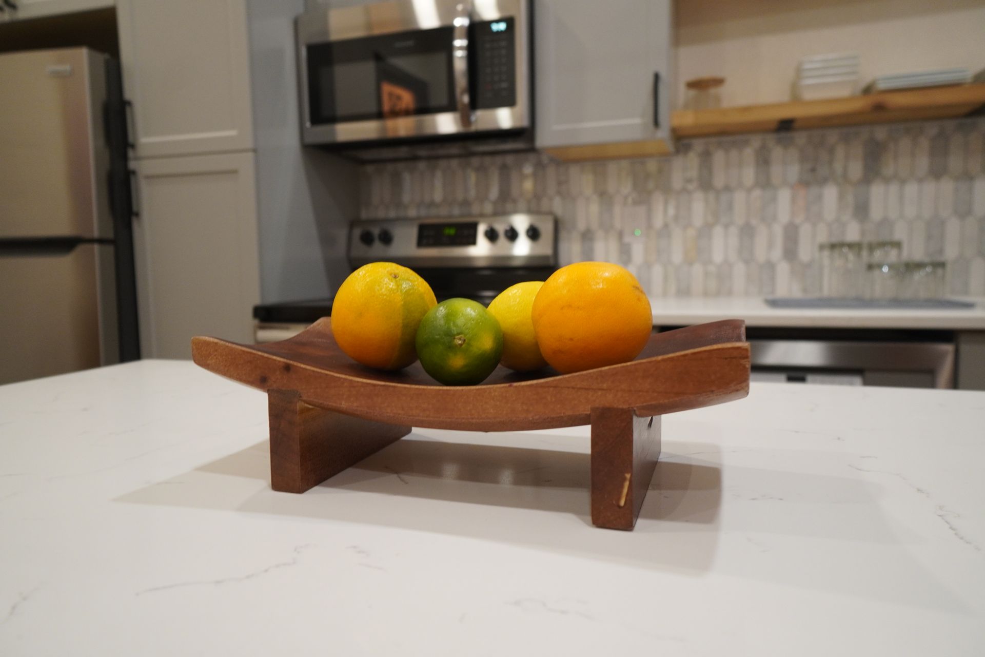 Wooden fruit bowl with oranges and limes on a white countertop in a kitchen.