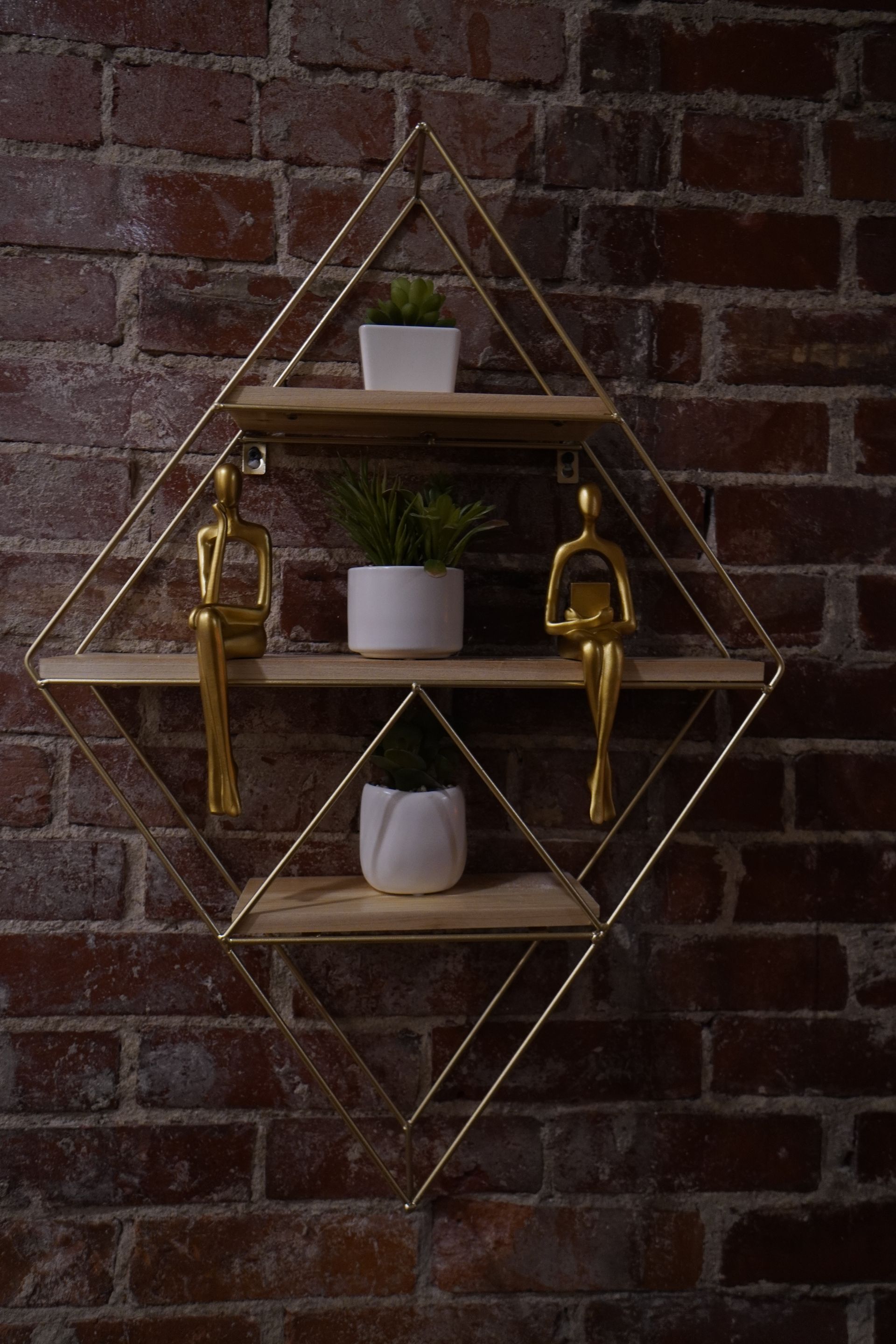 Diamond-shaped gold shelf on a brick wall, displaying plants and gold statues.