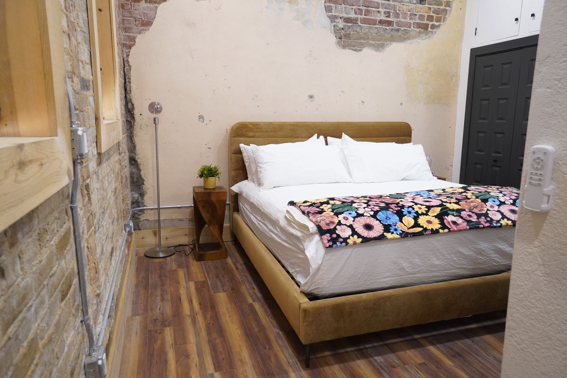 Bedroom with bed, exposed brick wall, wood flooring, and gold-toned bed frame and blanket.