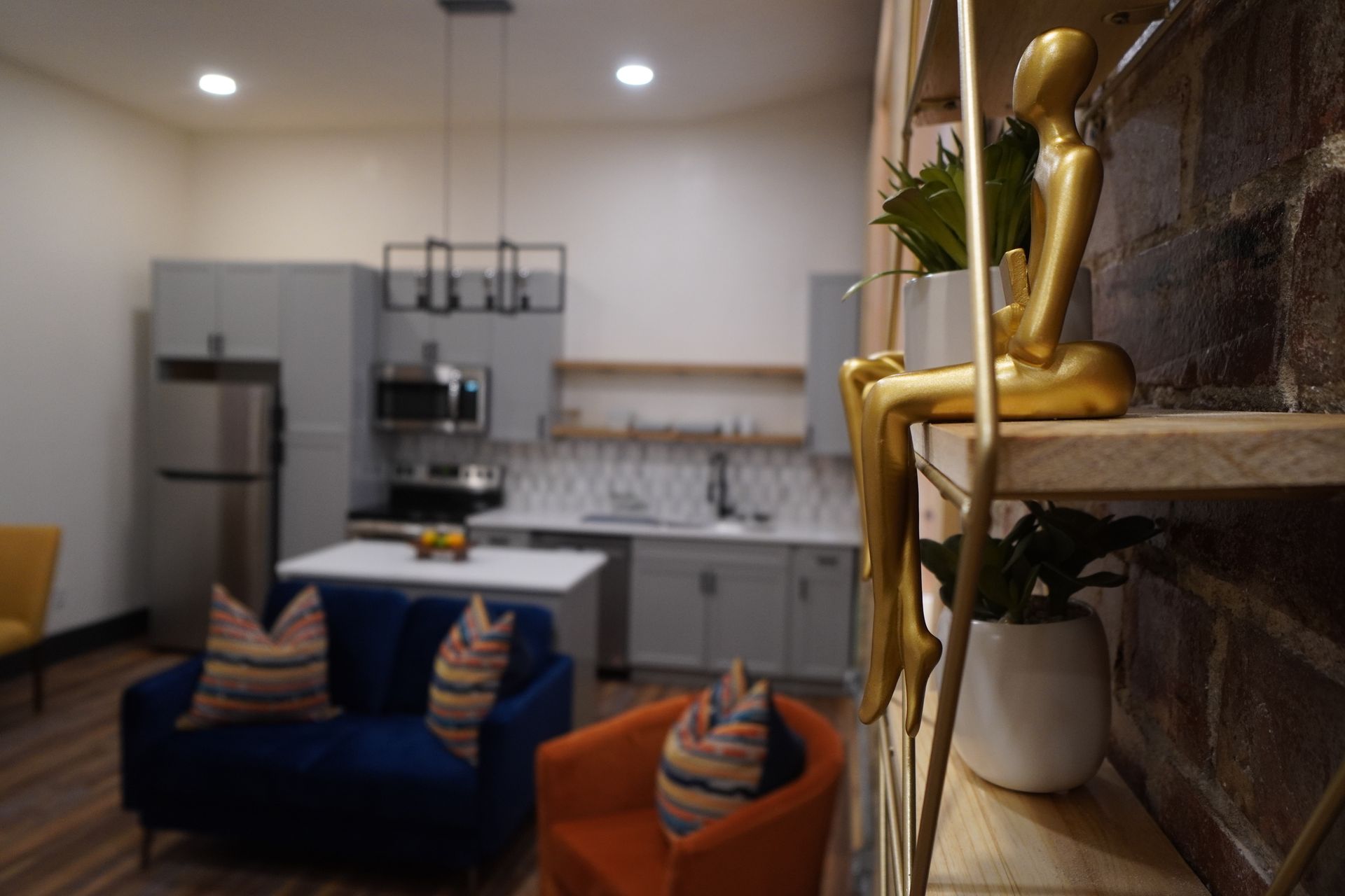 Gold statue on shelf in front of a living space with blue couch, orange chair, and kitchen.