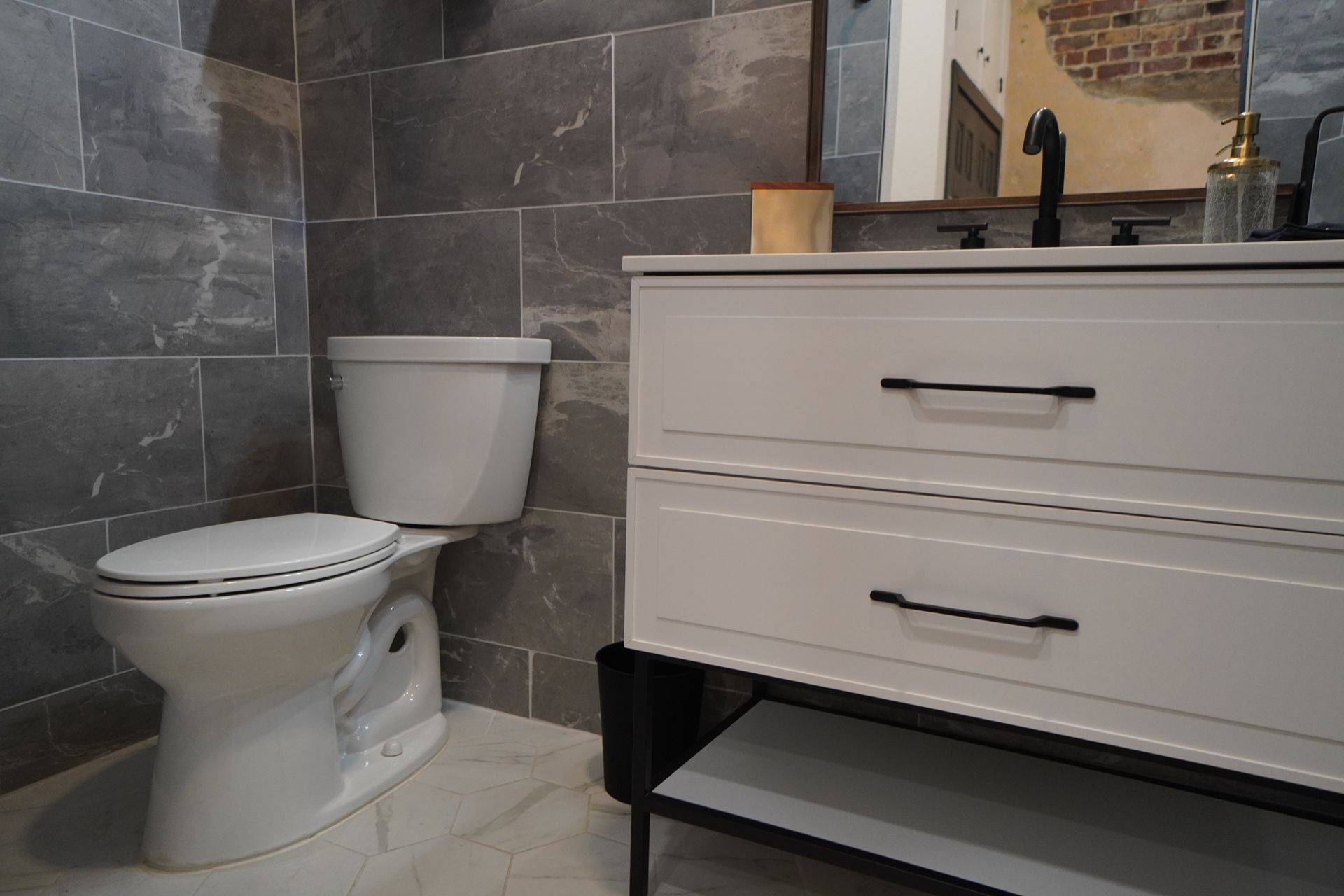 Bathroom with white vanity, toilet, gray tile, and black fixtures.