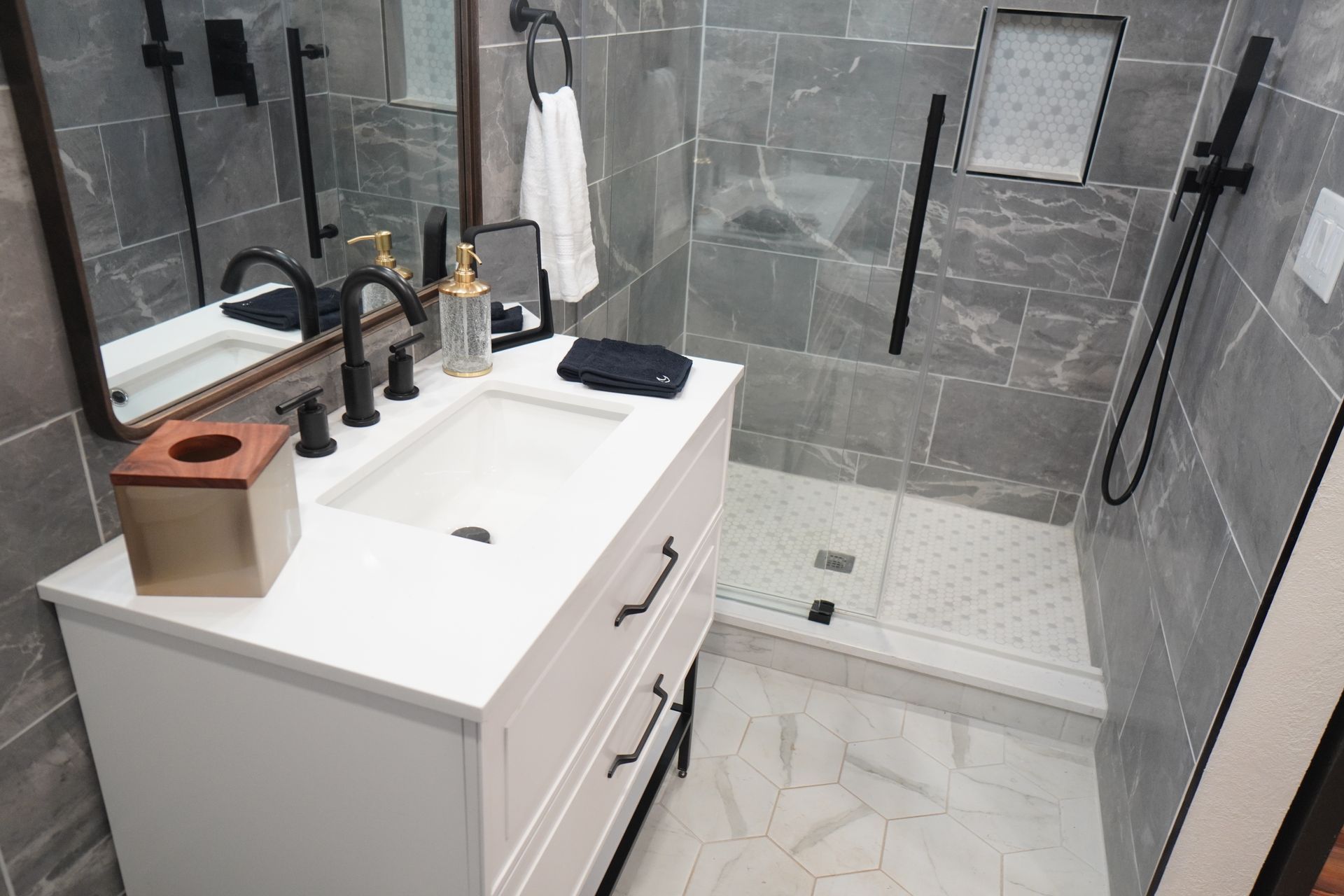 Bathroom with white vanity, black fixtures, gray tiled walls, and a shower.