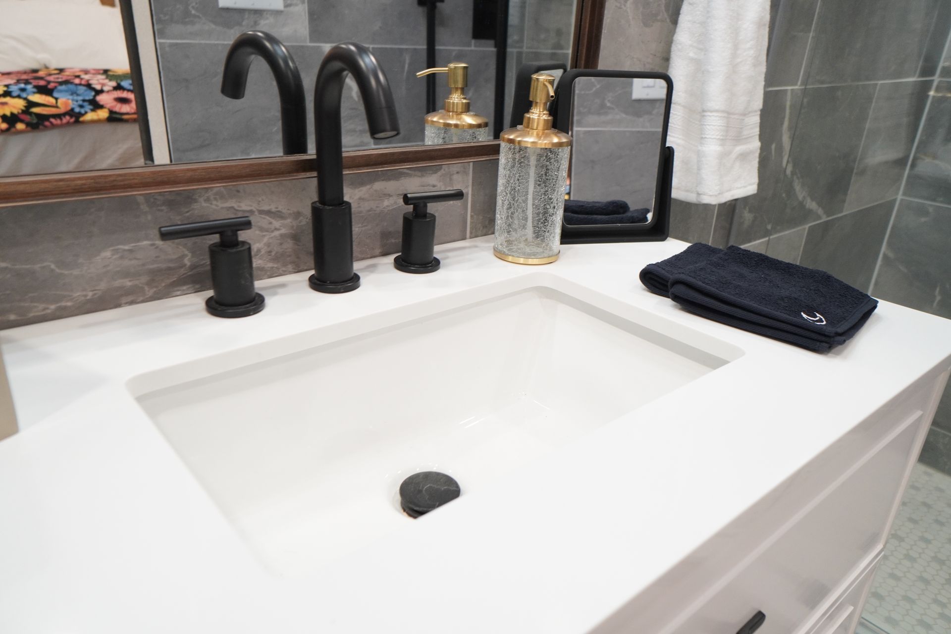 White bathroom vanity with black faucet and accessories; towel and soap dispenser are present.
