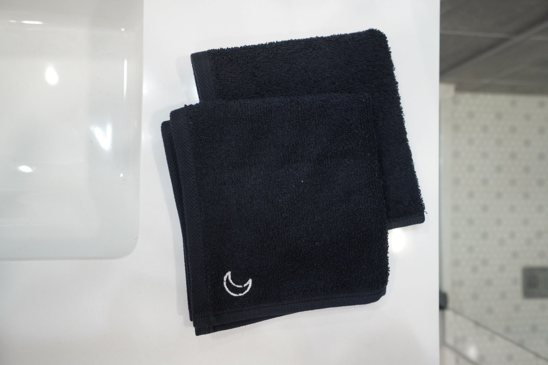 Two folded black hand towels with a crescent moon logo, sitting on a white surface.